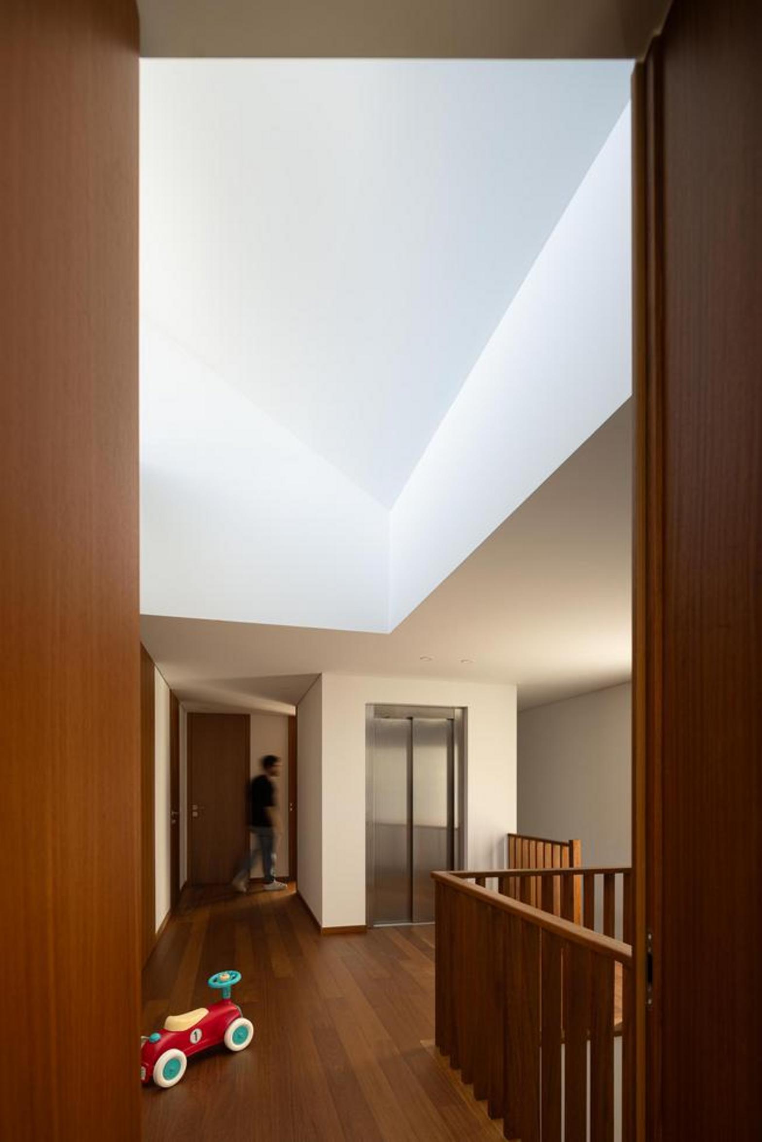 Hall de distribuição com pavimento em madeira e paredes brancas. Painéis de madeira e elevador, banhados por iluminação zenital superior — Duas Casas em Guimarães arquitectura Félix Arquitectos fotografia Ivo Tavares