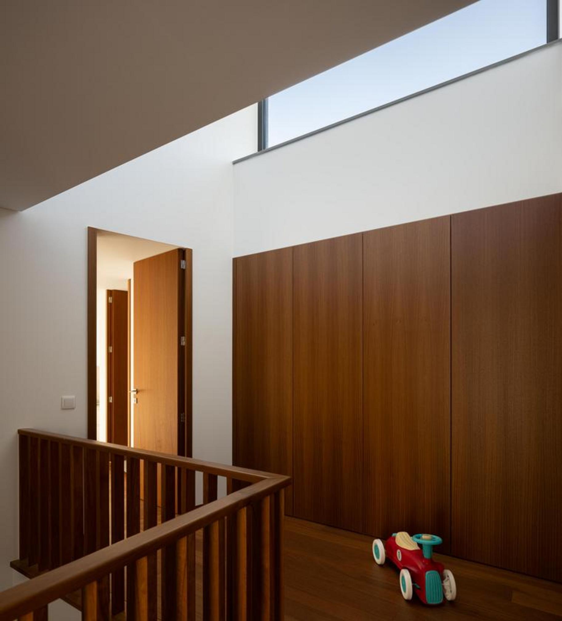 Corredor superior com pavimento e armários em madeira. Guarda-corpos de escada em madeira e iluminação zenital através de vão horizontal — Duas Casas em Guimarães arquitectura Félix Arquitectos fotografia Ivo Tavares