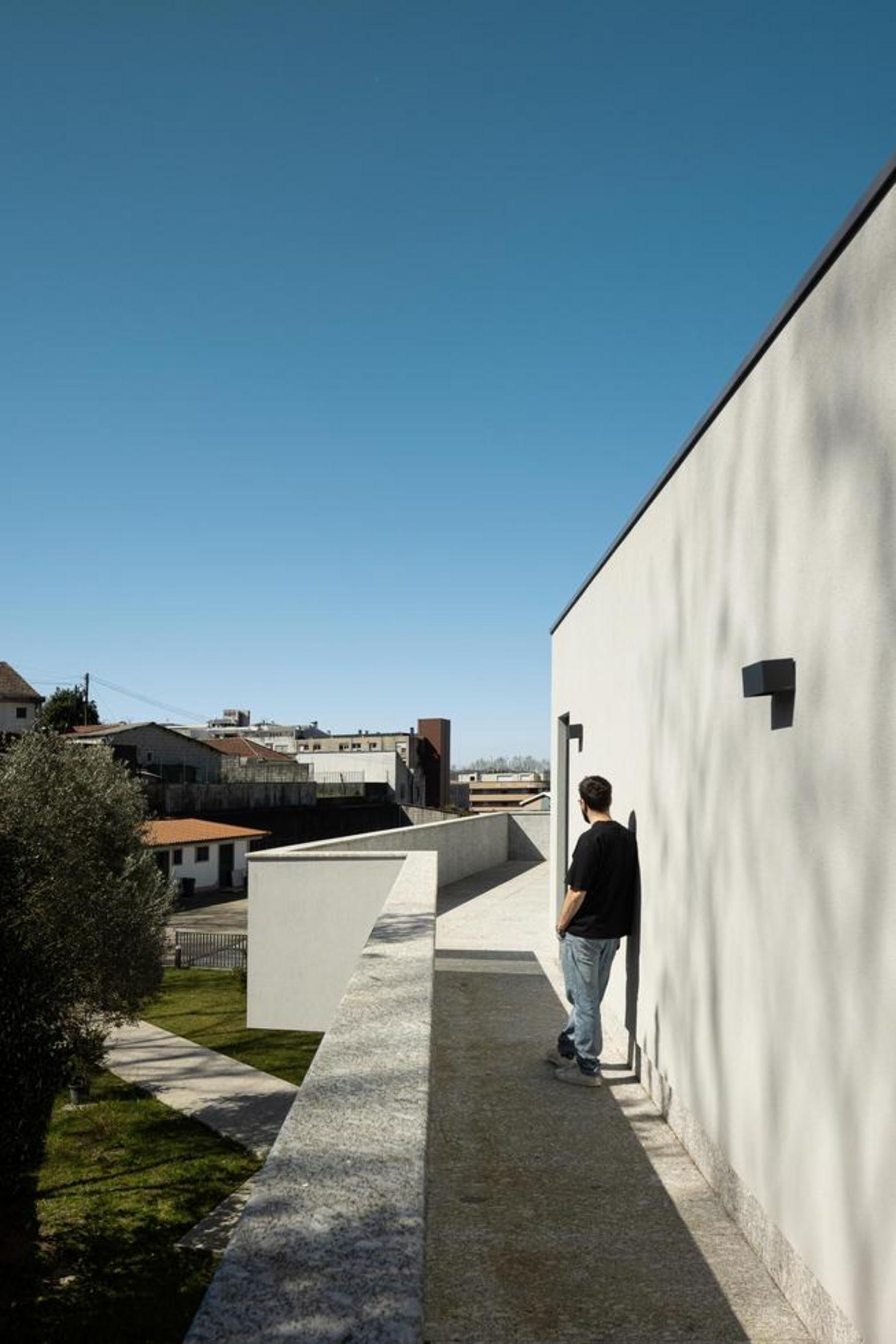 Varanda exterior com pavimento e guarda-corpos em pedra clara. Fachada branca com candeeiro preto. Vista para o casario urbano sob céu azul — Duas Casas em Guimarães arquitectura Félix Arquitectos fotografia Ivo Tavares