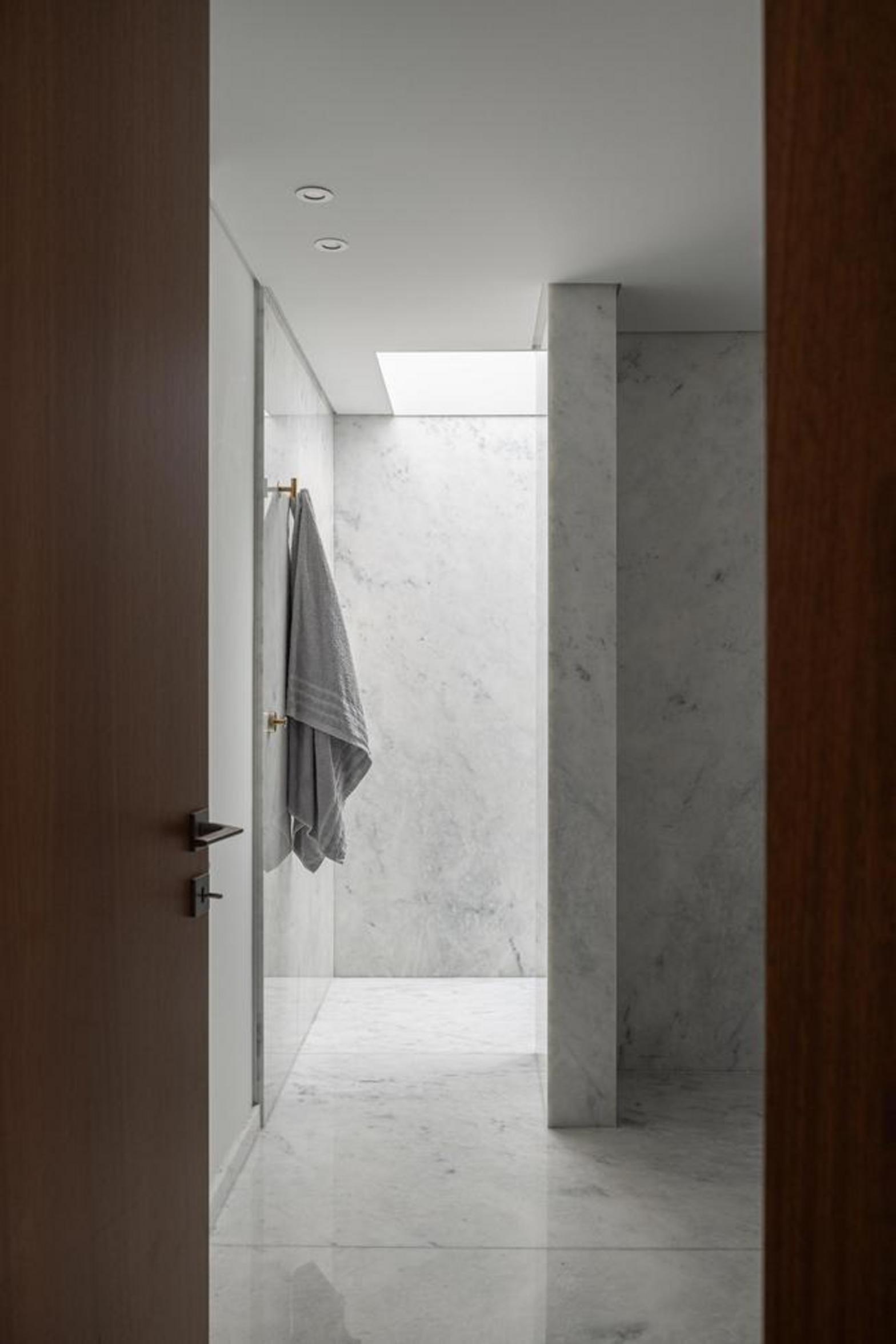 Interior de casa de banho revestido a mármore branco com veios cinzentos. Iluminação zenital suave realça a textura da pedra — Duas Casas em Guimarães arquitectura Félix Arquitectos fotografia Ivo Tavares