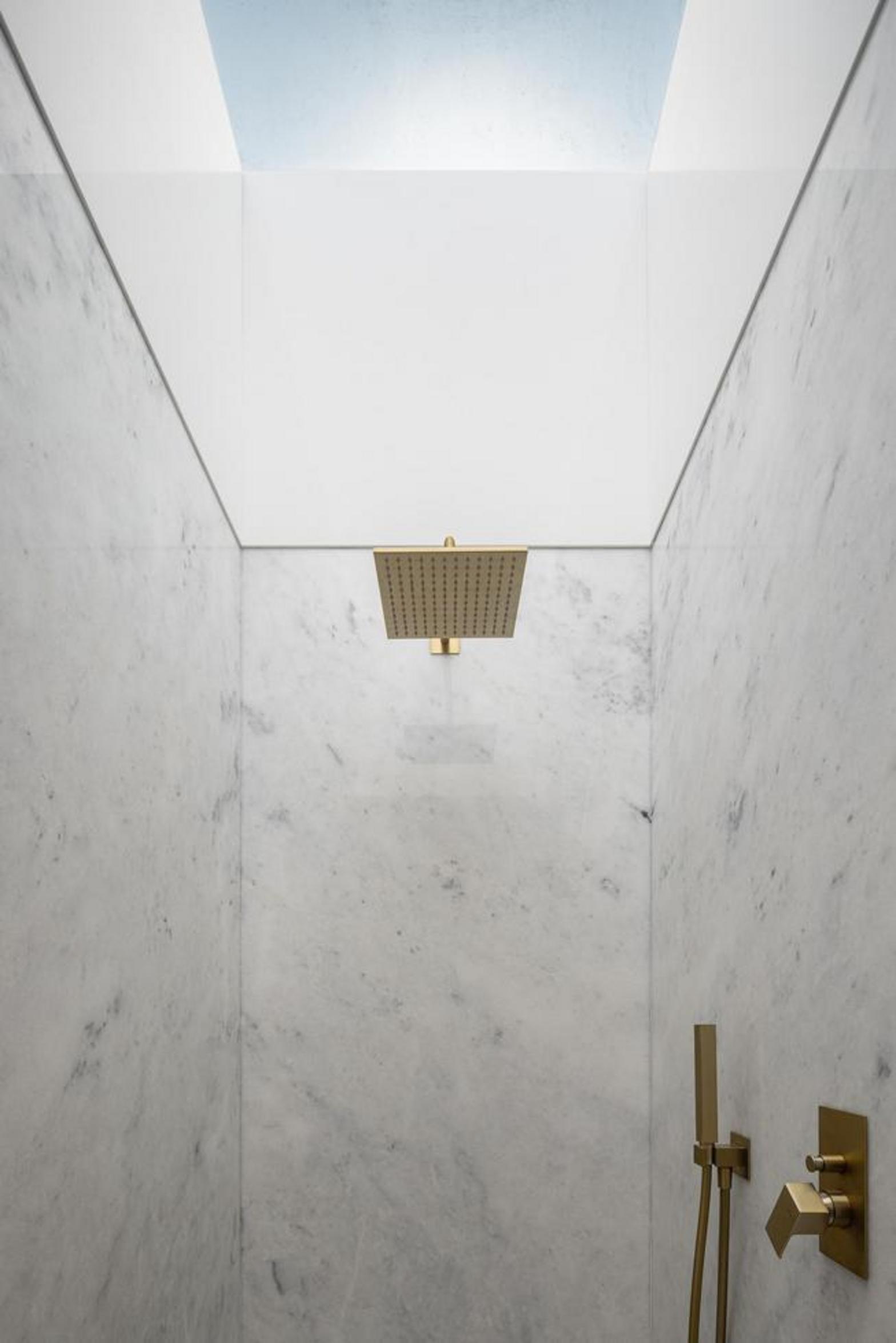 Duche com interior revestido a mármore branco e chuveiro dourado. Iluminação zenital cria um espaço vertical e minimalista — Duas Casas em Guimarães arquitectura Félix Arquitectos fotografia Ivo Tavares