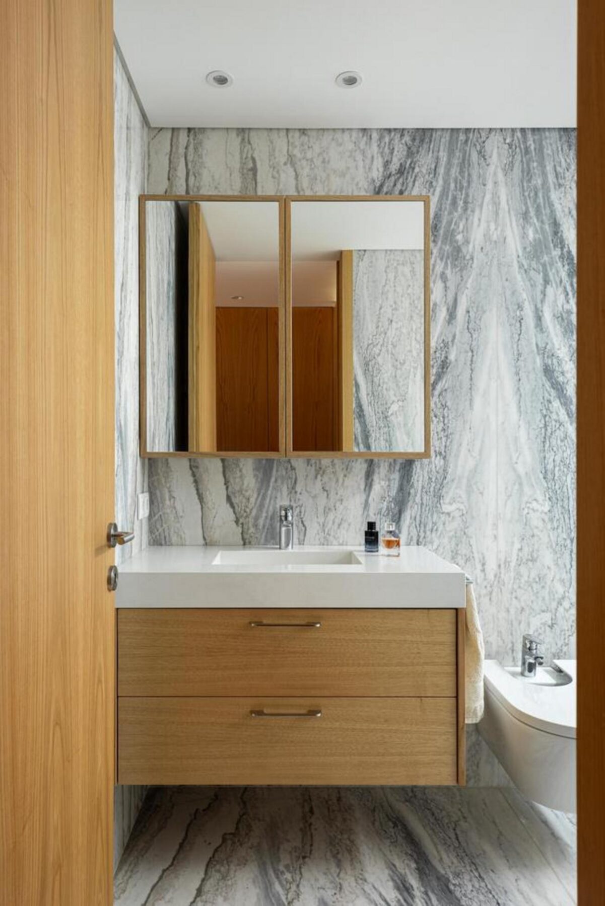 Cozinha de planta aberta, com ilha central e armários em madeira clara, conectada à sala de jantar e com vista para o exterior. — Duas casas em Guimarães arquitectura felixARQS – Daniel Félix Arquitectos fotografia Ivo Tavares