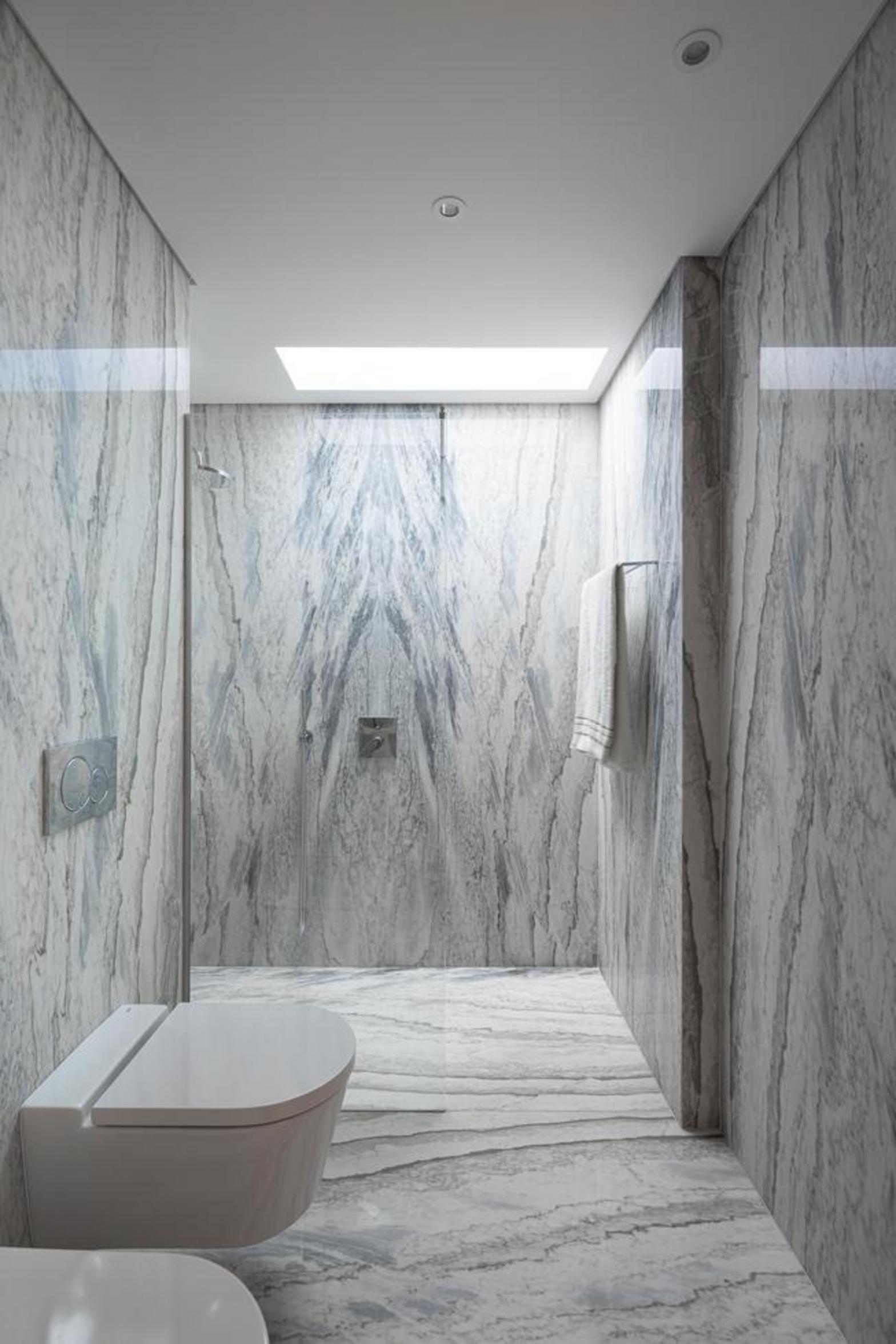 Casa de banho com interior revestido a mármore de veios marcados. Sanita suspensa e iluminação zenital, criando um espaço alongado — Duas Casas em Guimarães arquitectura Félix Arquitectos fotografia Ivo Tavares