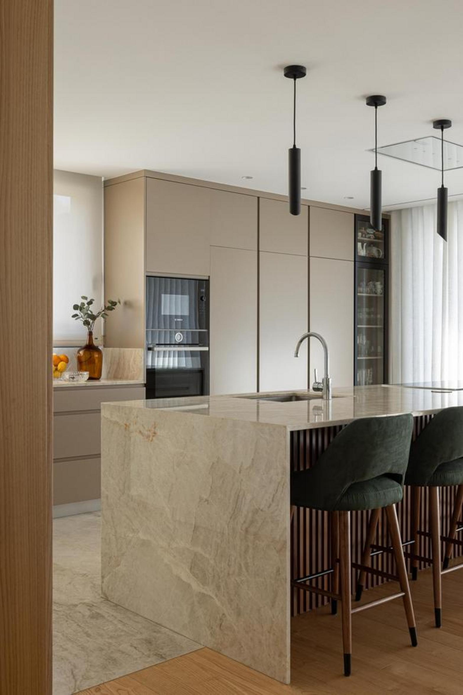 Cozinha com ilha central em mármore bege. Armários em tom neutro e candeeiros suspensos pretos. Pavimento em madeira e pedra — Duas Casas em Guimarães arquitectura Félix Arquitectos fotografia Ivo Tavares