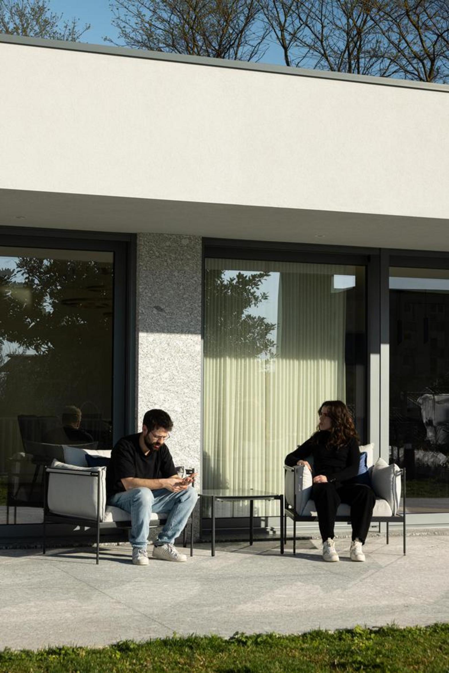 Terraço exterior com pavimento em pedra clara e grandes vãos envidraçados. Fachada branca e embasamento em pedra, com mobiliário de exterior — Duas Casas em Guimarães arquitectura Félix Arquitectos fotografia Ivo Tavares