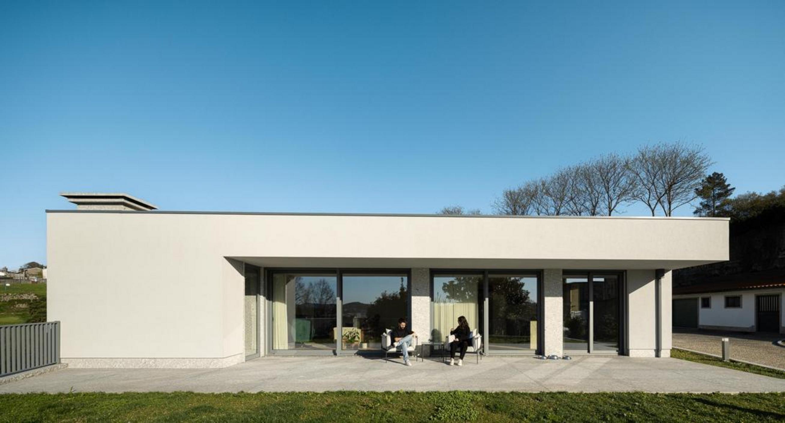 Fachada posterior da moradia térrea. Volume branco e embasamento em pedra. Grandes vãos envidraçados e terraço exterior em pedra — Duas Casas em Guimarães arquitectura Félix Arquitectos fotografia Ivo Tavares
