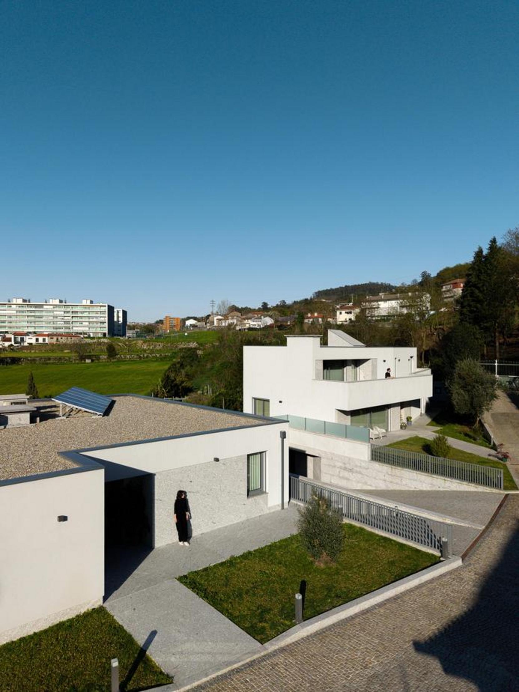 Vista aérea do complexo de moradias. Volumes brancos e embasamento em pedra. Coberturas planas, integrando-se na topografia acentuada — Duas Casas em Guimarães arquitectura Félix Arquitectos fotografia Ivo Tavares