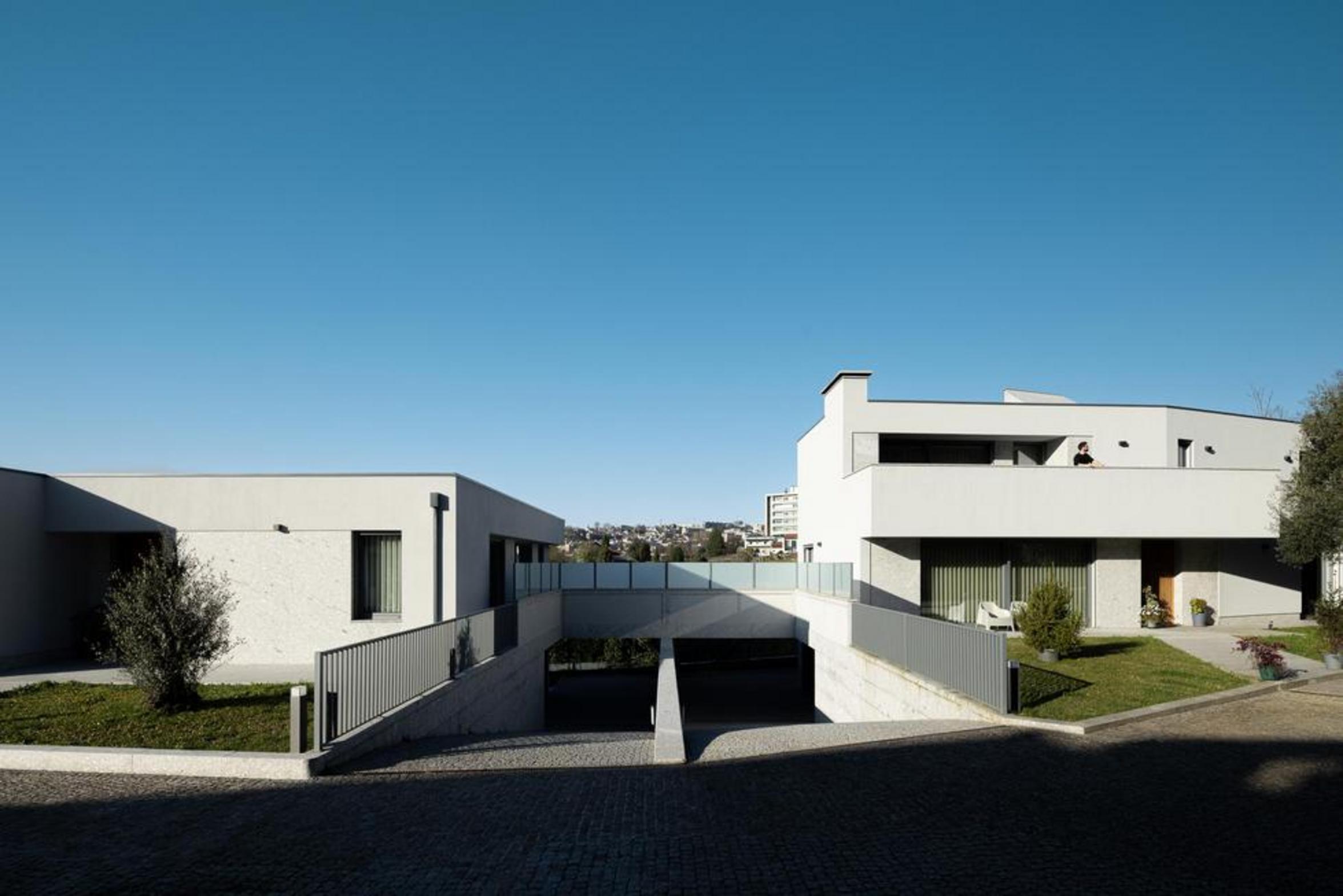 Fachada frontal das moradias. Volumes brancos e embasamento em pedra. Rampa de acesso à garagem e guarda-corpos metálicos — Duas Casas em Guimarães arquitectura Félix Arquitectos fotografia Ivo Tavares
