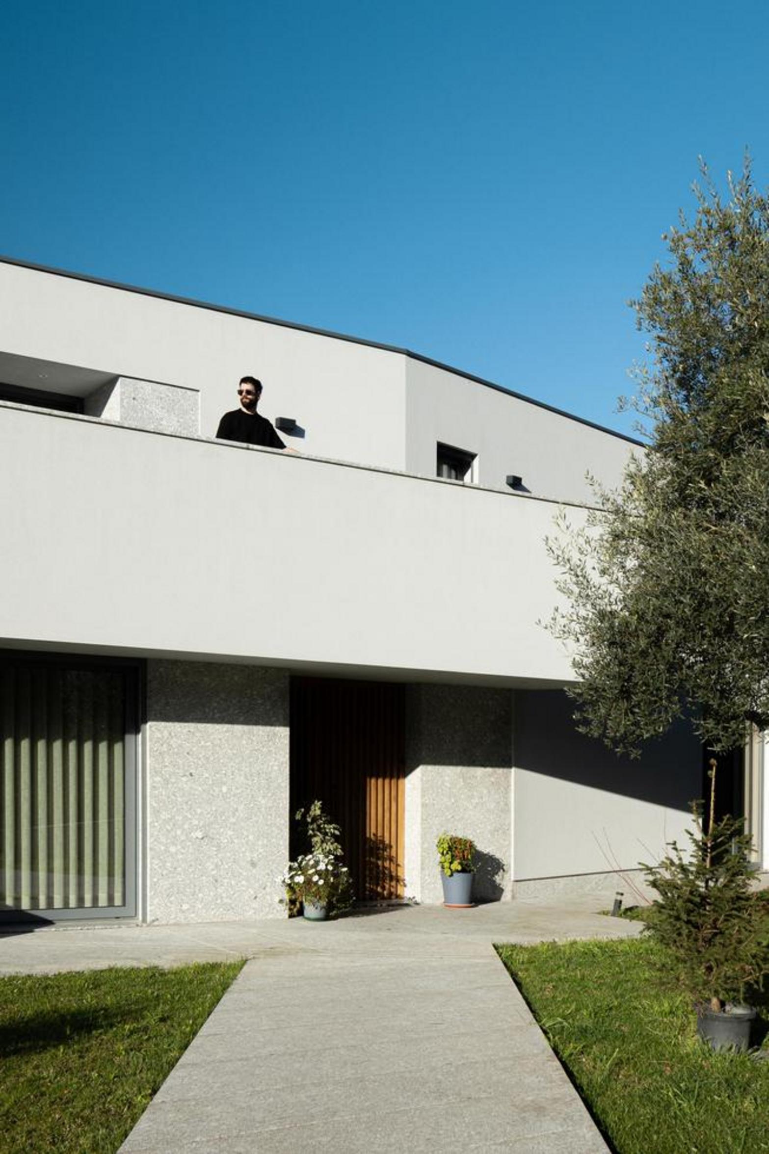 Fachada principal da moradia. Volumes brancos e embasamento em pedra. Entrada recuada e varanda superior, com caminho em betão — Duas Casas em Guimarães arquitectura Félix Arquitectos fotografia Ivo Tavares