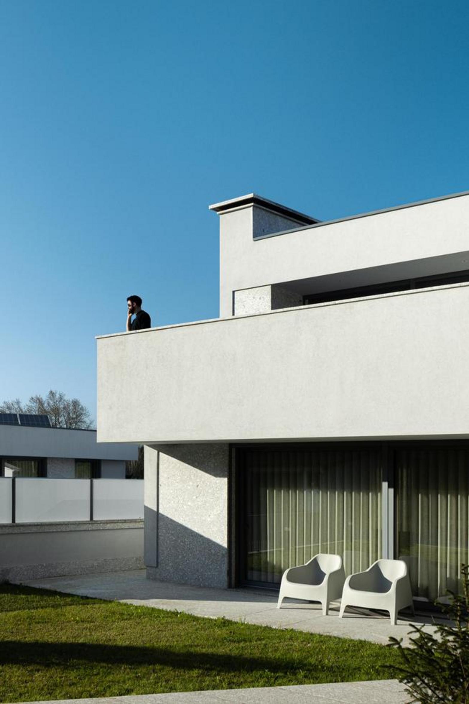 Fachada lateral da moradia de dois pisos. Volumes brancos e embasamento em pedra. Varanda superior e mobiliário de exterior no jardim — Duas Casas em Guimarães arquitectura Félix Arquitectos fotografia Ivo Tavares