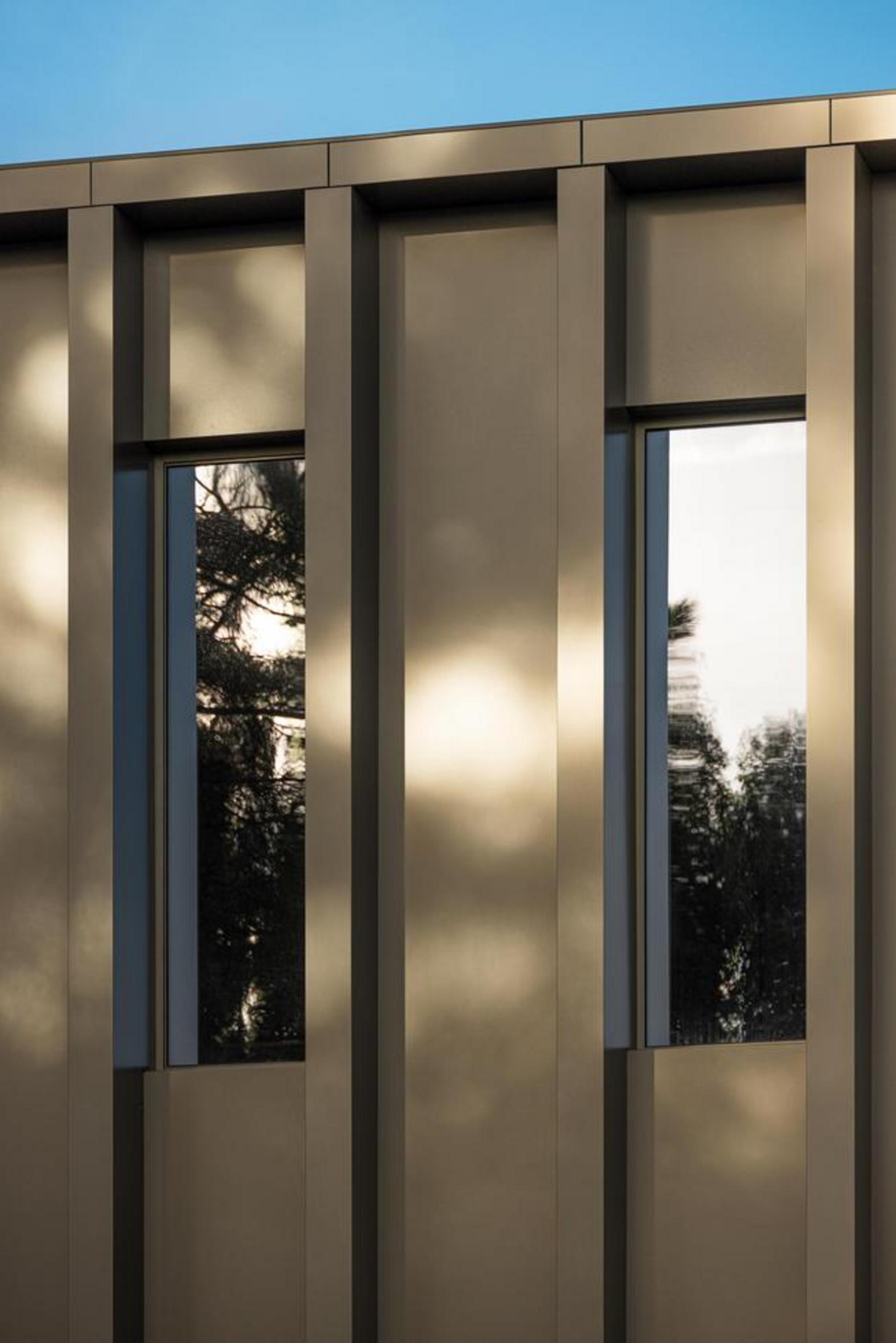 Detalhe da fachada com brise-soleil verticais em painel metálico bronze e vãos envidraçados que refletem a paisagem — Novo Edifício-Sede PRF arquitectura Impare Arquitectura fotografia Ivo Tavares