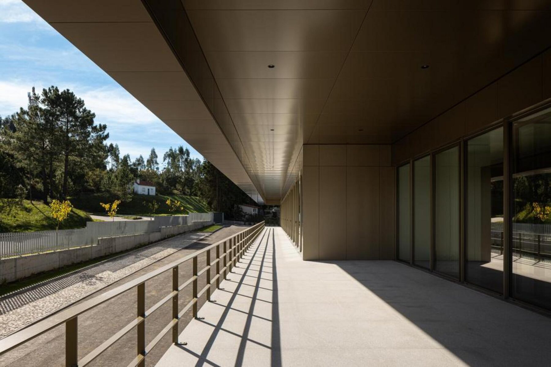 Corredor de acesso aos escritórios, com paredes brancas e pavimento contínuo, conduzindo a uma área de trabalho iluminada naturalmente. — EDIFÍCIO-SEDE PRF arquitectura Impare Arquitectura fotografia Ivo Tavares