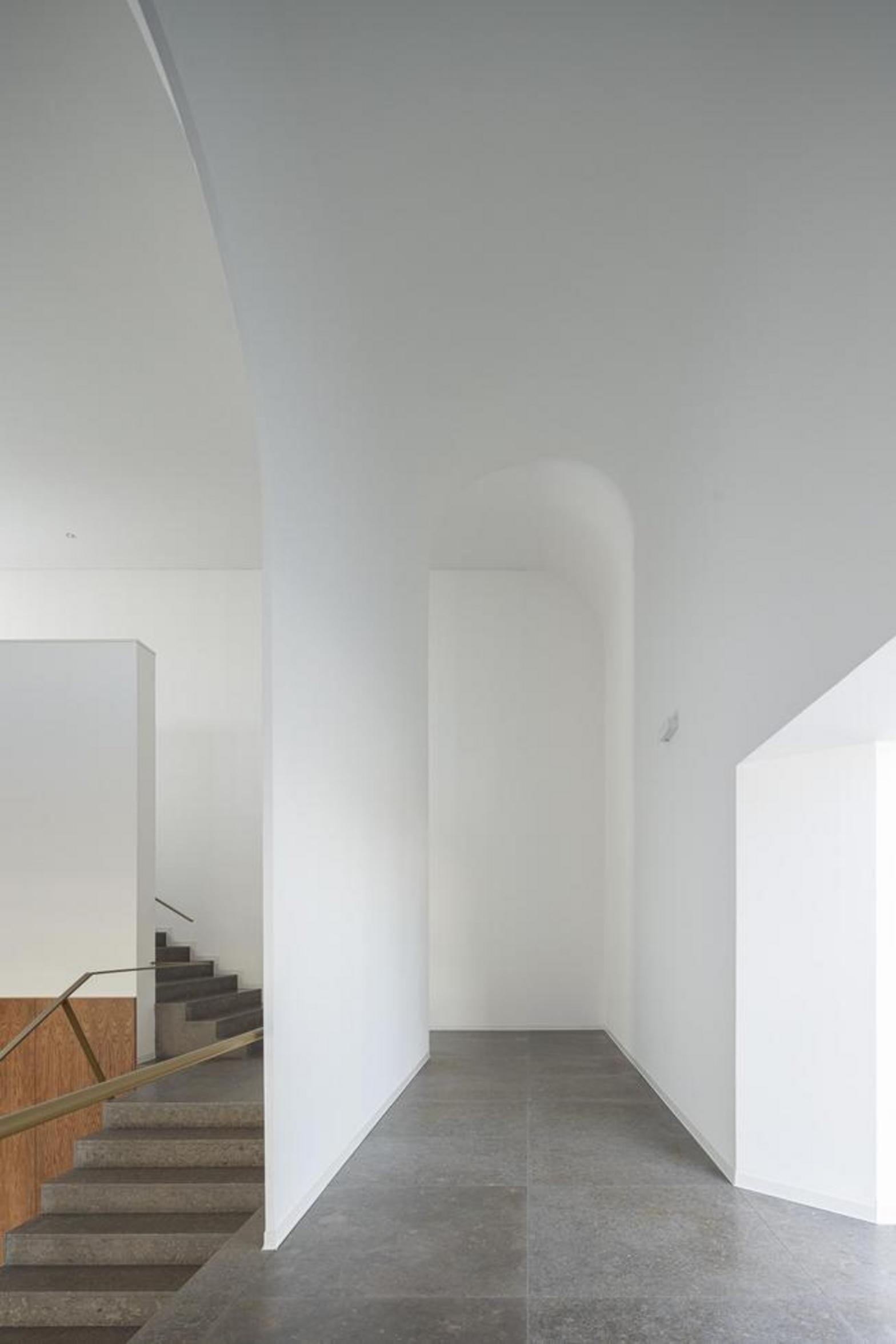 Corredor interior com pavimento em grés escuro, paredes brancas e sucessão de vãos em arco, criando profundidade — Novo Edifício-Sede PRF arquitectura Impare Arquitectura fotografia Ivo Tavares