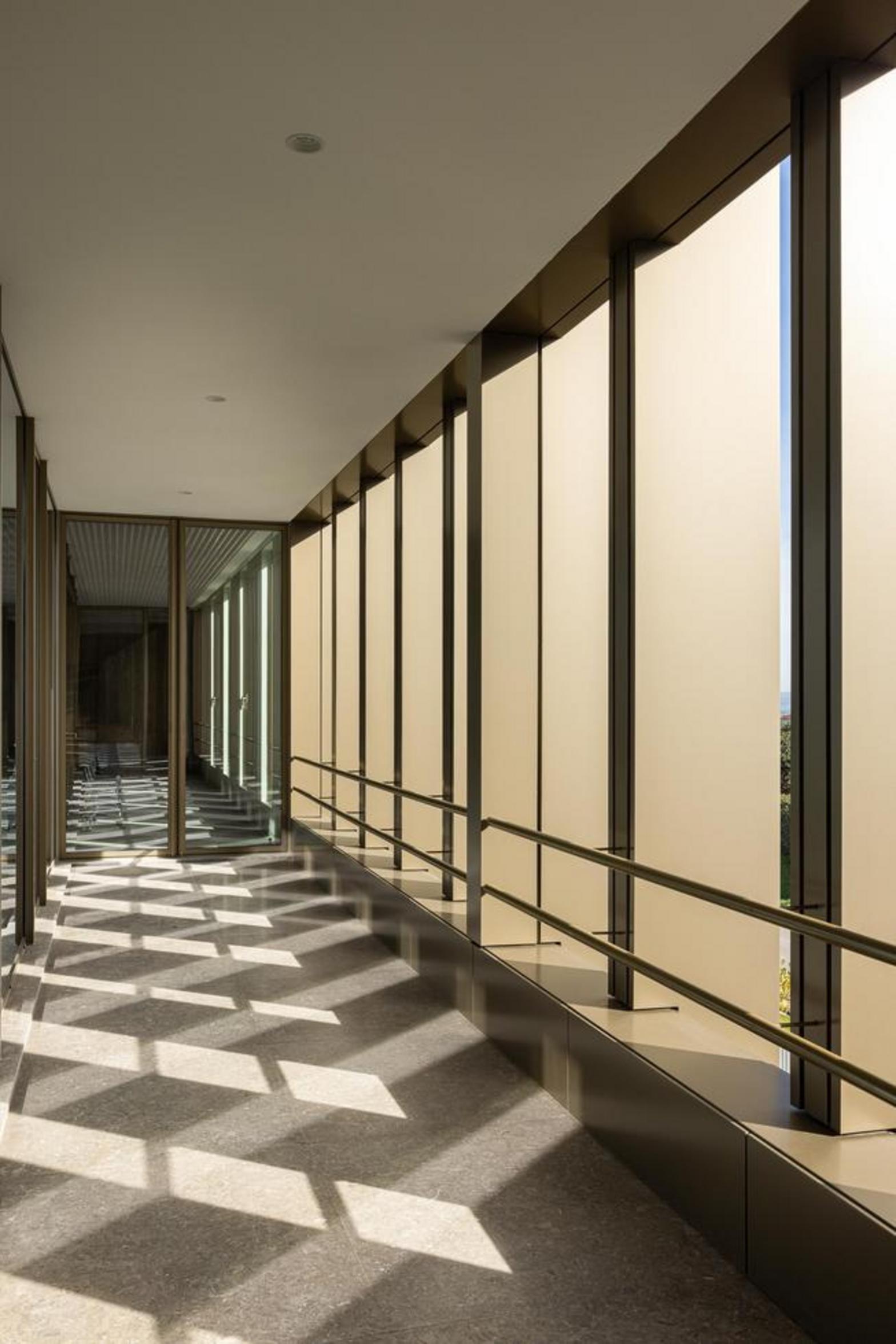 Corredor com pavimento em pedra clara, paredes envidraçadas com brise-soleil verticais e jogo de luz e sombra — Novo Edifício-Sede PRF arquitectura Impare Arquitectura fotografia Ivo Tavares