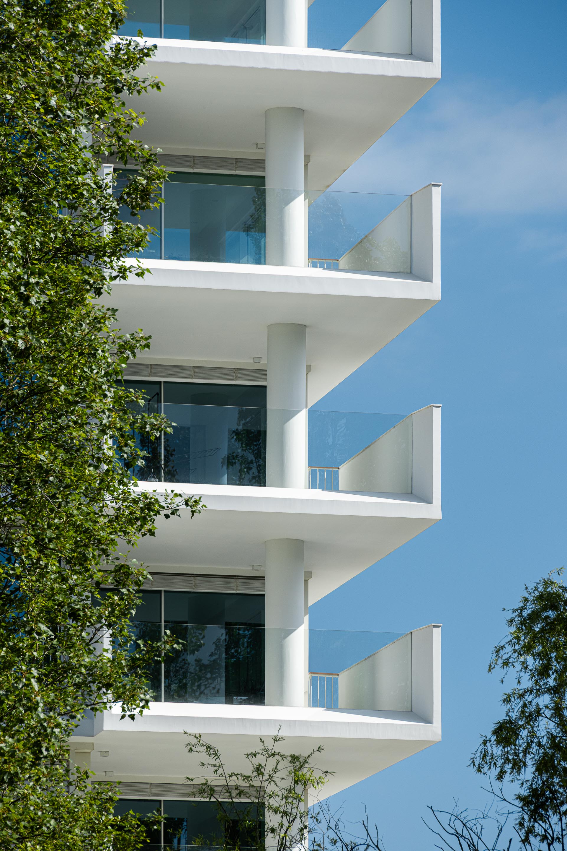 Detalhe de varandas em consola com lajes finas e guardas de vidro estrutural. Pilares cilíndricos em reboco branco — Edifício Natura arquitectura Visioarq Arquitectos fotografia Ivo Tavares