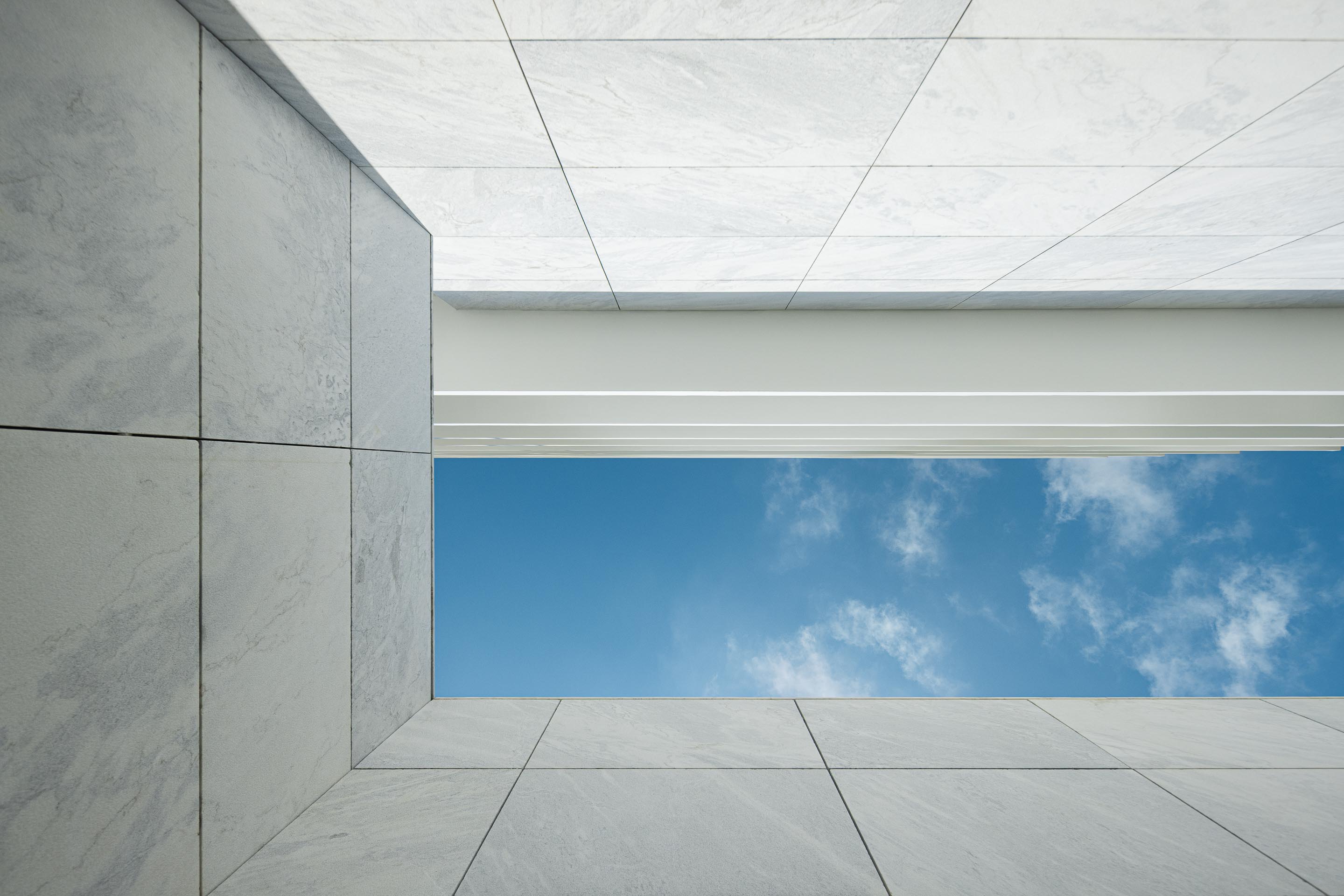 Vão quadrado de luz zenital em mármore branco, revelando o céu azul com nuvens — Edifício Natura arquitectura Visioarq Arquitectos fotografia Ivo Tavares