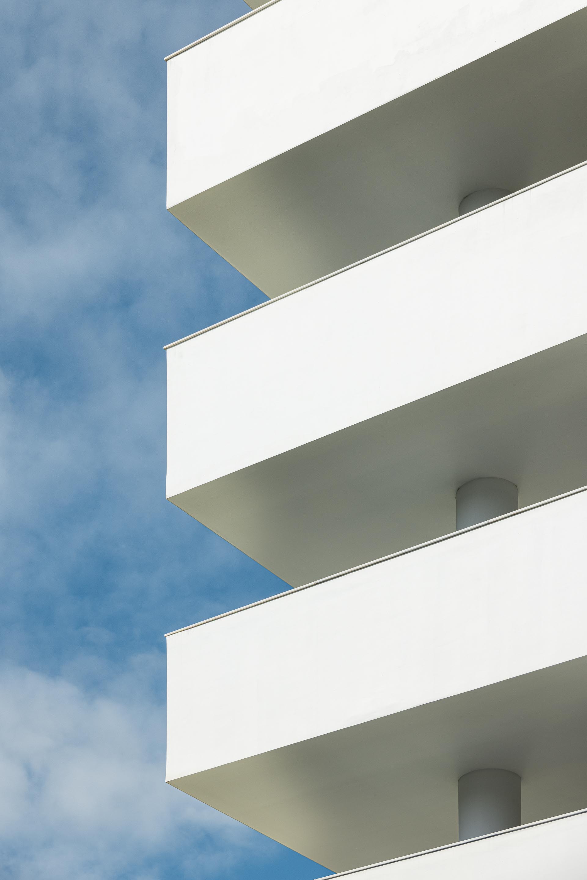 Detalhe de varandas em consola com lajes finas em reboco branco, suportadas por pilares cilíndricos recuados — Edifício Natura arquitectura Visioarq Arquitectos fotografia Ivo Tavares
