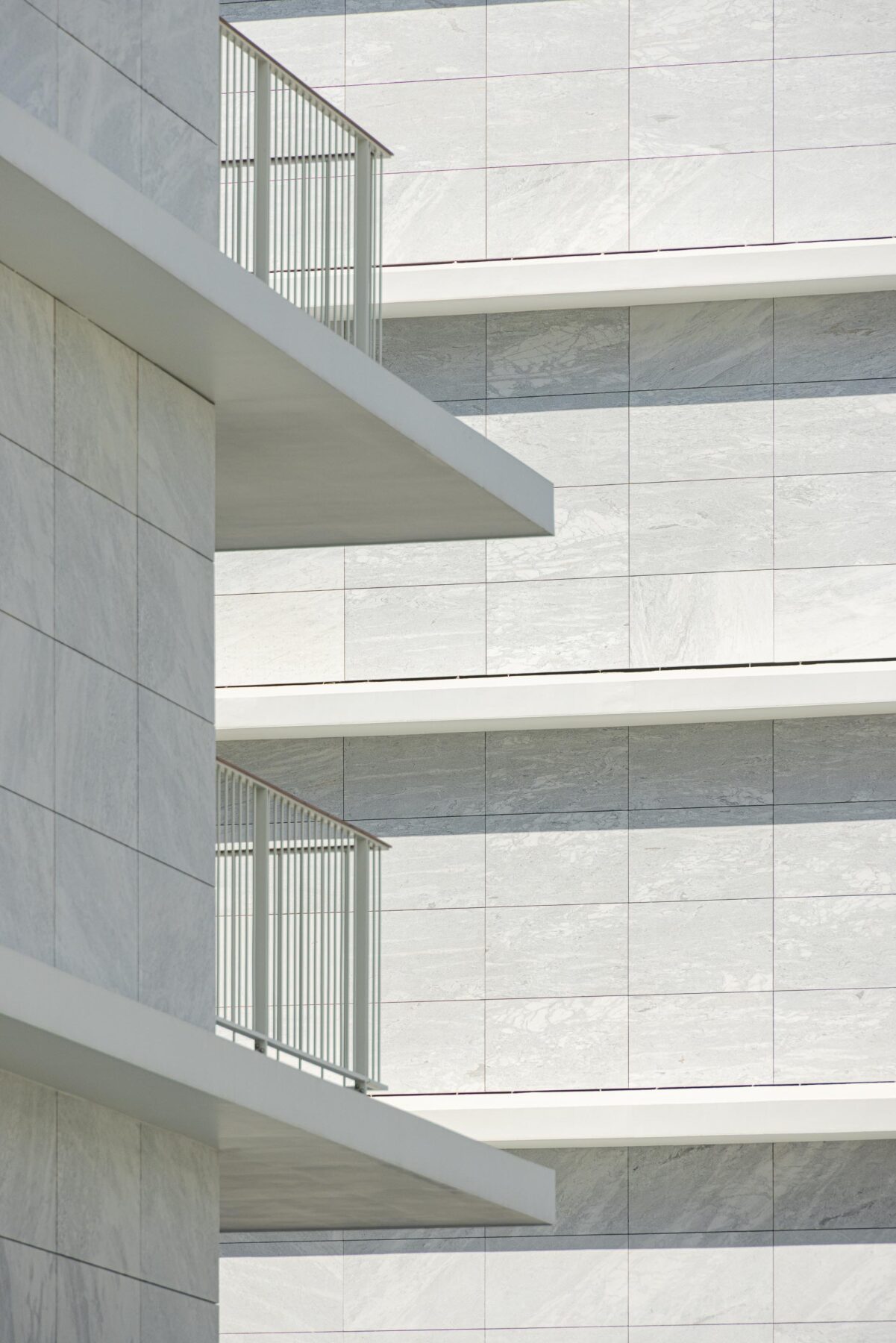 Fachada revestida a mármore branco, com varandas em consola de reboco branco e guardas metálicas. Sombras projetadas — Edifício Natura arquitectura Visioarq Arquitectos fotografia Ivo Tavares