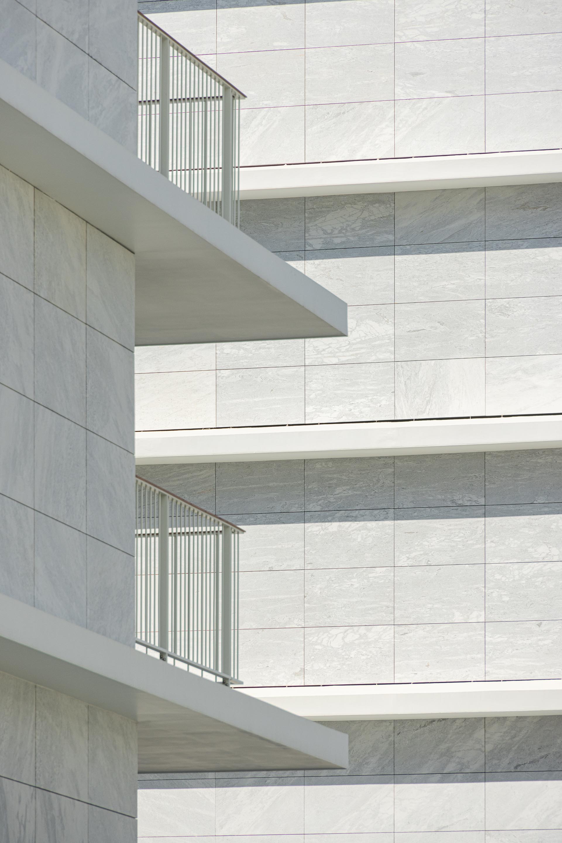 Fachada revestida a mármore branco, com varandas em consola de reboco branco e guardas metálicas. Sombras projetadas — Edifício Natura arquitectura Visioarq Arquitectos fotografia Ivo Tavares