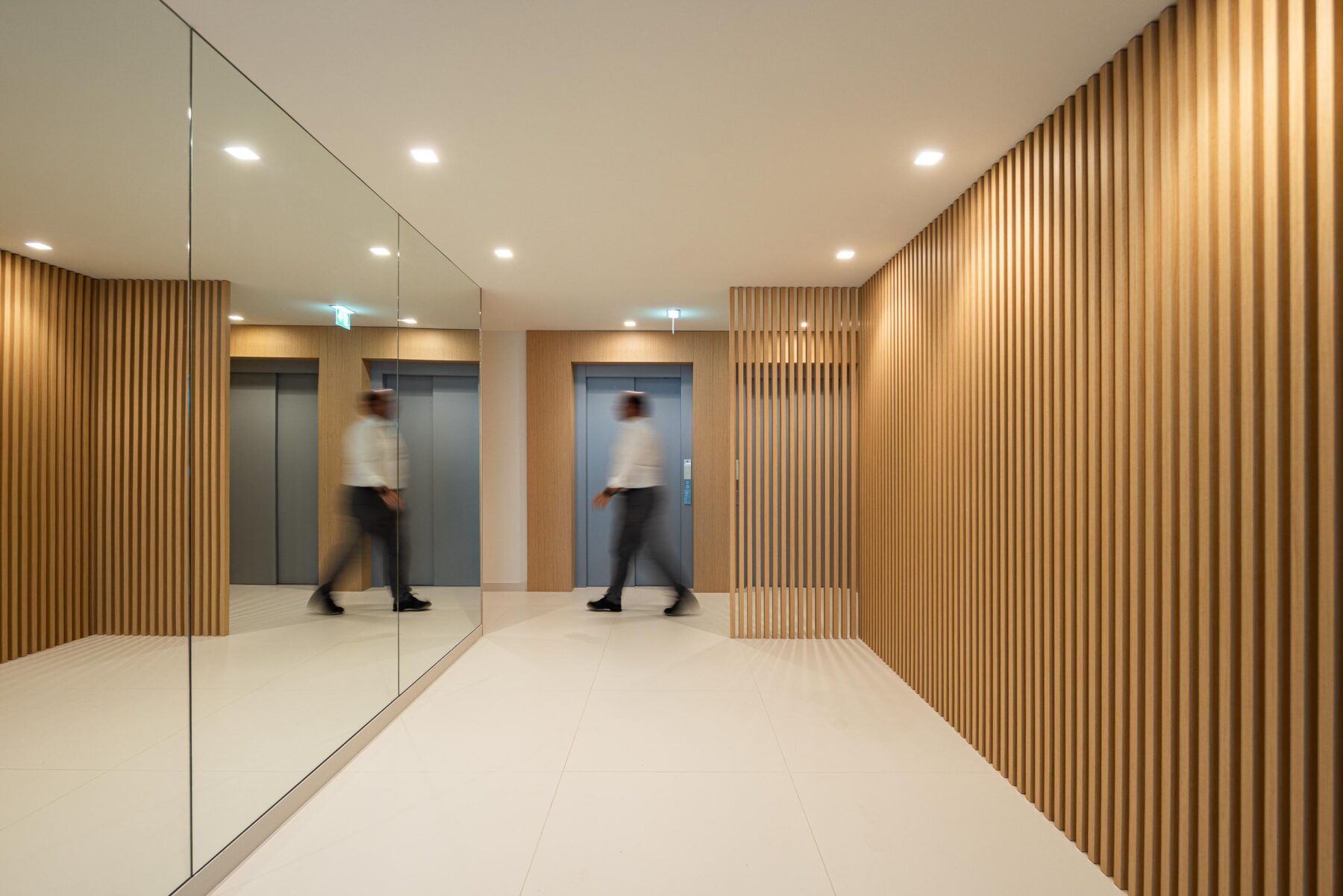 Hall de entrada com pavimento em cerâmica clara, painéis e ripado de madeira clara. Espelho e elevadores metálicos — Edifício Natura arquitectura Visioarq Arquitectos fotografia Ivo Tavares