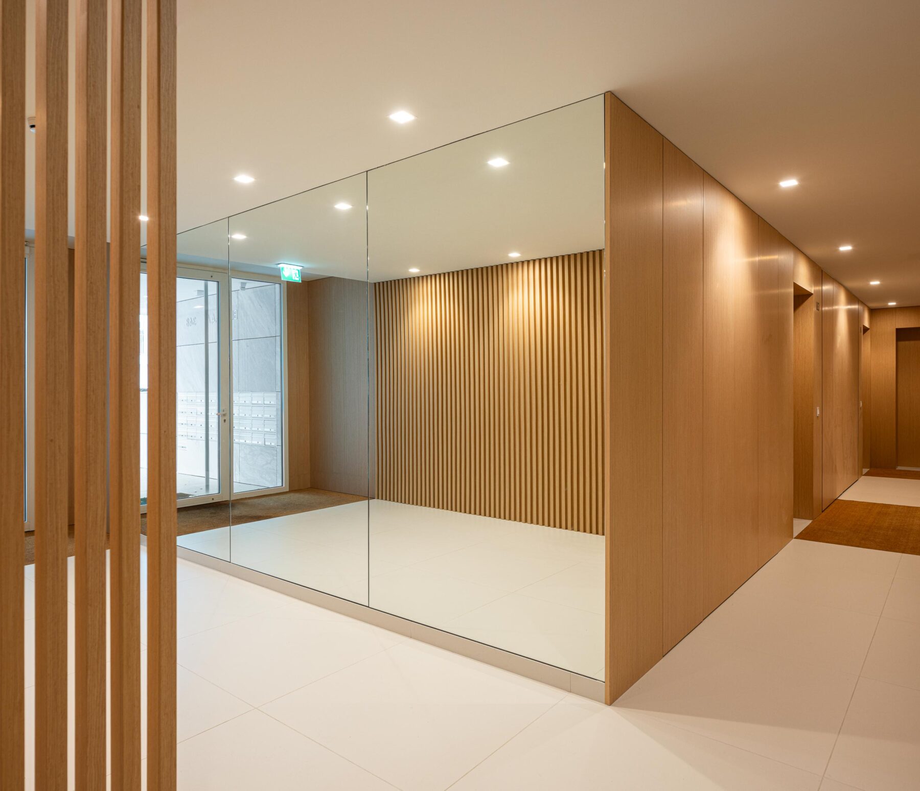Hall de entrada com pavimento em cerâmica clara, paredes revestidas a madeira clara e espelhos. Luz artificial embutida — Edifício Natura arquitectura Visioarq Arquitectos fotografia Ivo Tavares