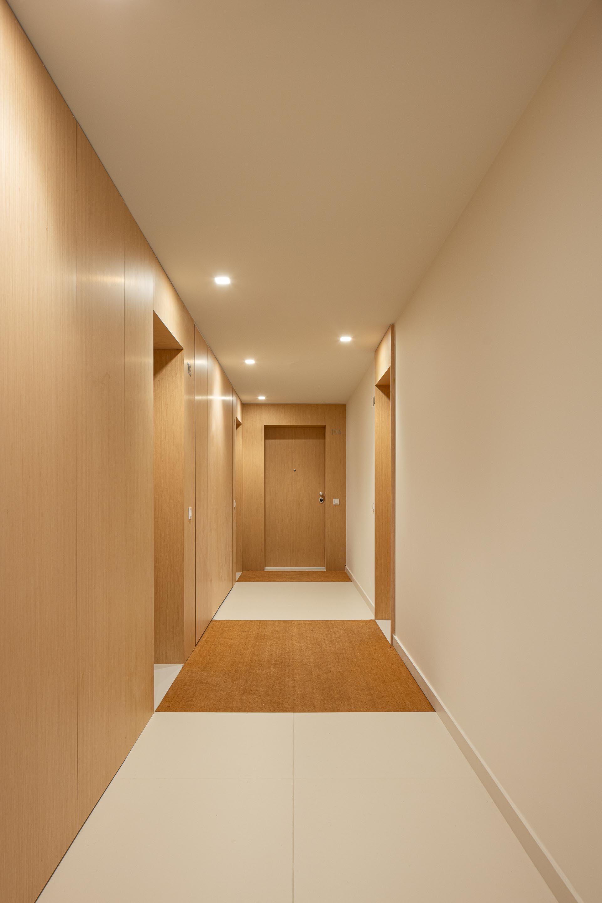 Corredor de acesso a apartamentos com pavimento em cerâmica clara, paredes em madeira clara e pintadas de branco — Edifício Natura arquitectura Visioarq Arquitectos fotografia Ivo Tavares