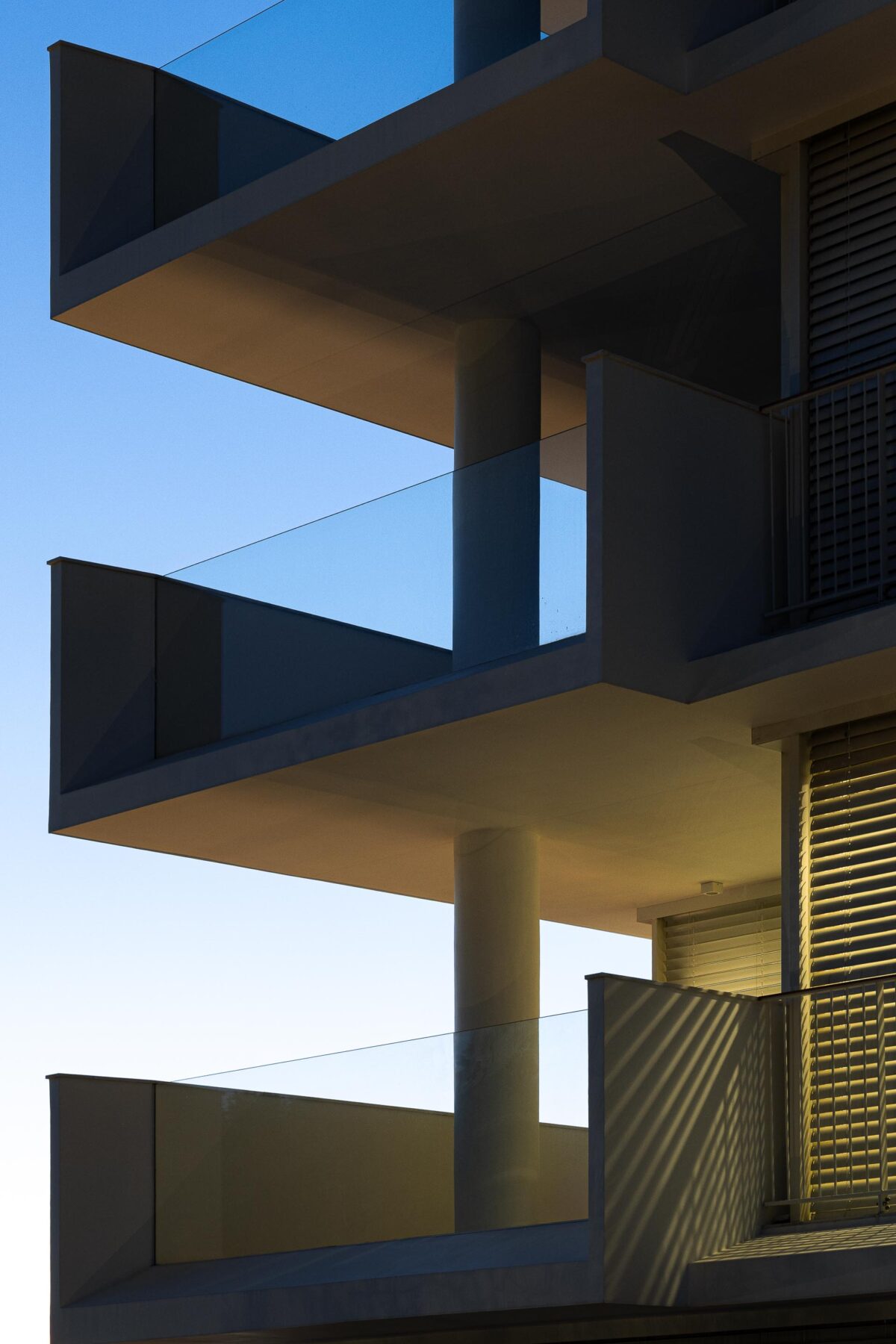 Detalhe de varandas em consola com lajes finas e guardas de vidro estrutural. Pilar cilíndrico e sombras projetadas — Edifício Natura arquitectura Visioarq Arquitectos fotografia Ivo Tavares