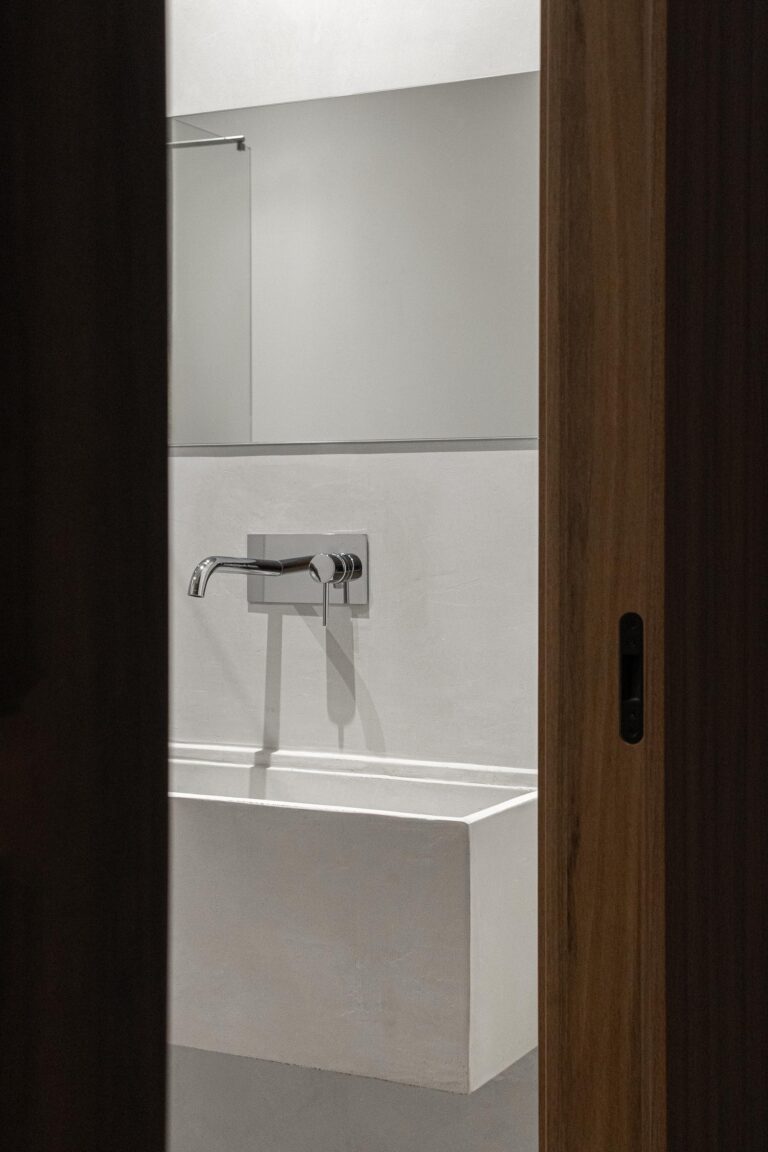 Detalhe da casa de banho com lavatório branco minimalista e torneira embutida na parede — Boutique Apartments arquitectura HPA fotografia Ivo Tavares