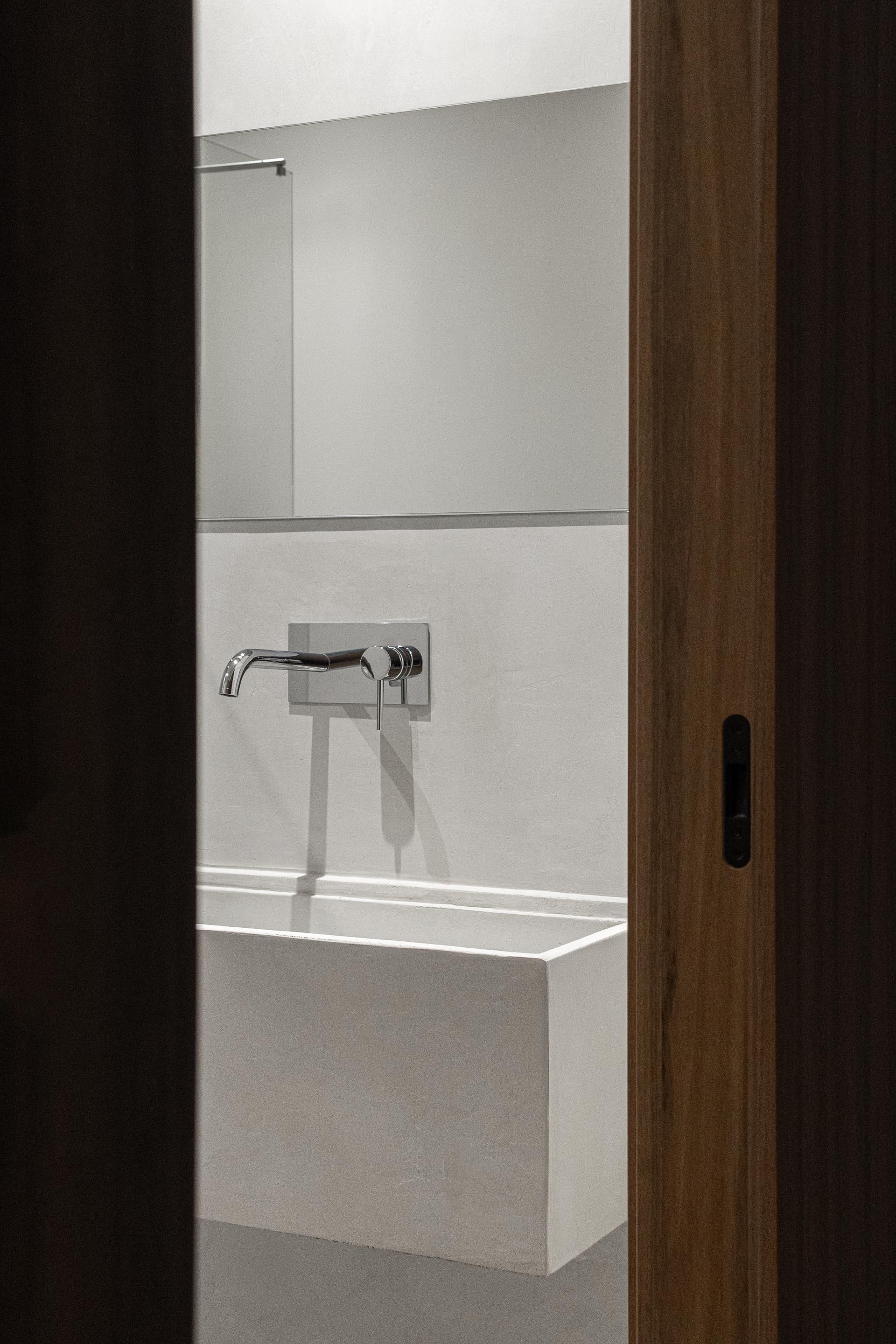 Detalhe da casa de banho com lavatório branco minimalista e torneira embutida na parede — Boutique Apartments arquitectura HPA fotografia Ivo Tavares