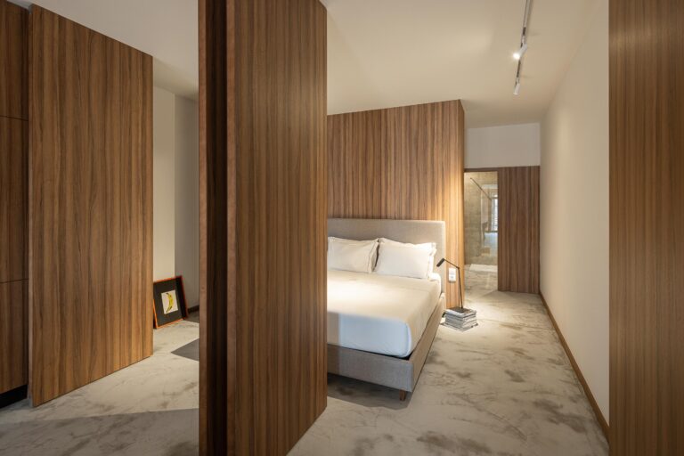 Quarto com pavimento em betão, painéis de madeira e cama de casal com cabeceira estofada — Boutique Apartments arquitectura HPA fotografia Ivo Tavares