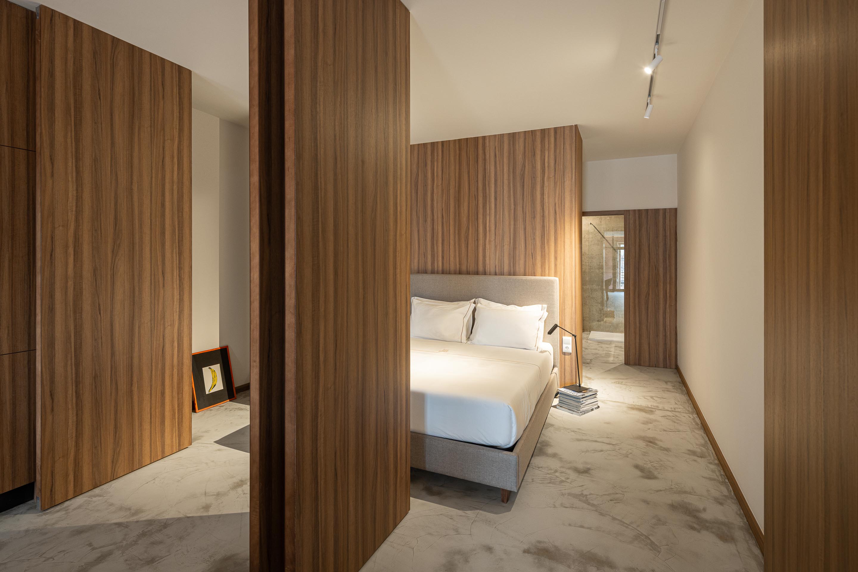 Quarto com pavimento em betão, painéis de madeira e cama de casal com cabeceira estofada — Boutique Apartments arquitectura HPA fotografia Ivo Tavares