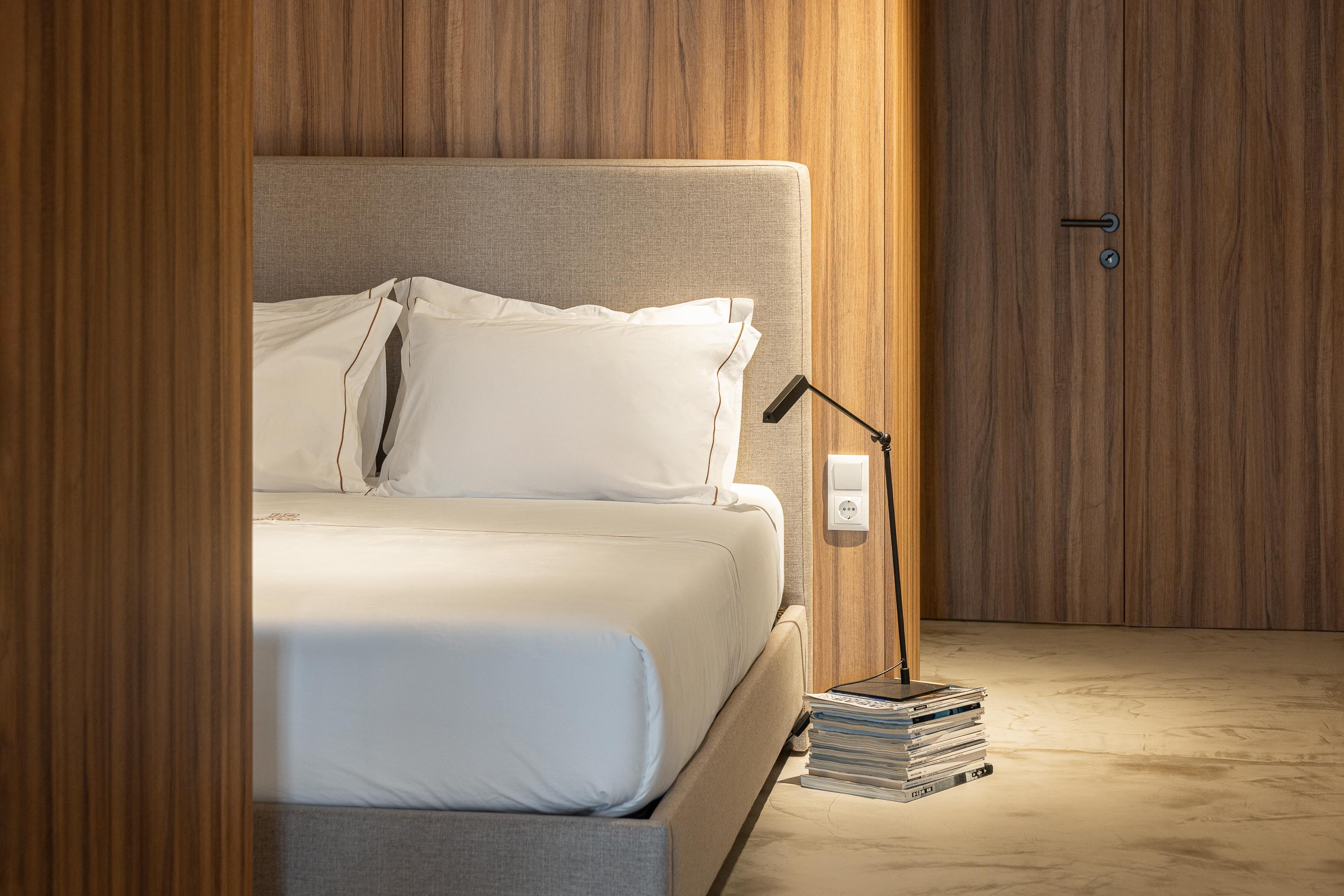 Detalhe do quarto com candeeiro de mesa sobre livros e revestimento em madeira — Boutique Apartments arquitectura HPA fotografia Ivo Tavares