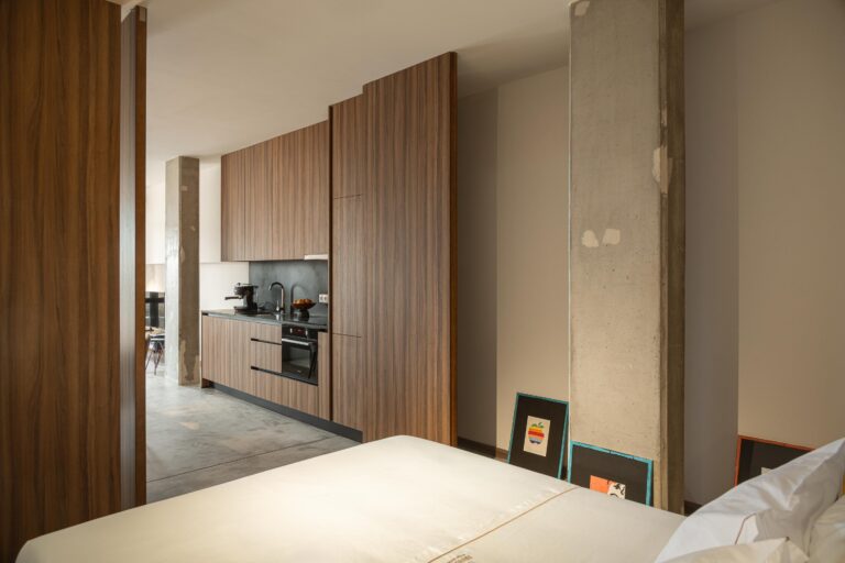Quarto e cozinha em plano aberto, com pilar em betão aparente e mobiliário em madeira — Boutique Apartments arquitectura HPA fotografia Ivo Tavares