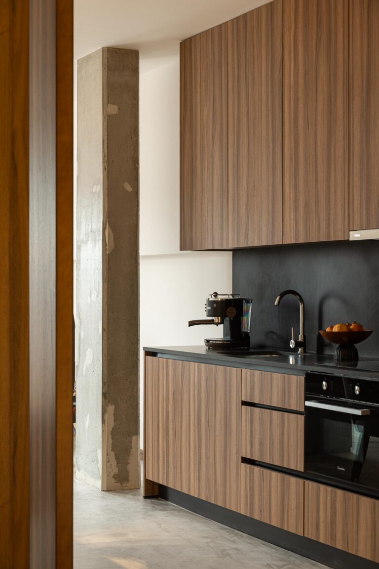 Detalhe da cozinha com armários em madeira, bancada preta e pilar em betão aparente — Boutique Apartments arquitectura HPA fotografia Ivo Tavares