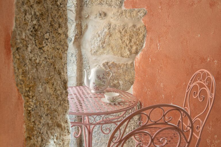 Detalhe da parede de pedra granítica e reboco rosa, com mesa e cadeira metálicas cor-de-rosa — Boutique Apartments arquitectura HPA fotografia Ivo Tavares