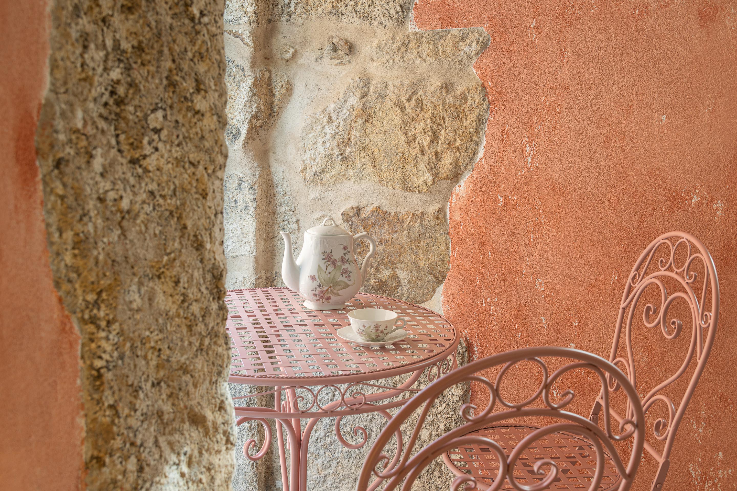Detalhe da parede de pedra granítica e reboco rosa, com mesa e cadeira metálicas cor-de-rosa — Boutique Apartments arquitectura HPA fotografia Ivo Tavares