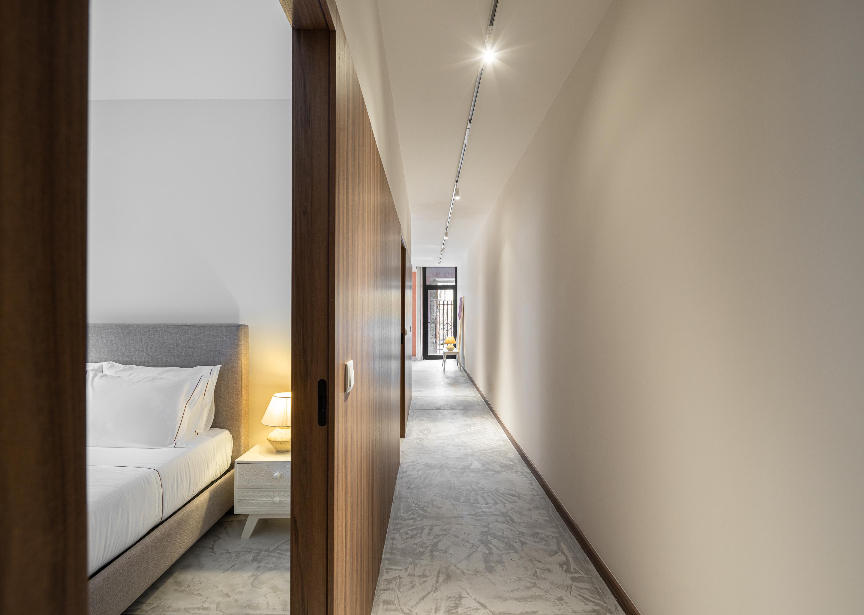 Corredor longo com pavimento em betão, paredes claras e porta de madeira — Boutique Apartments arquitectura HPA fotografia Ivo Tavares