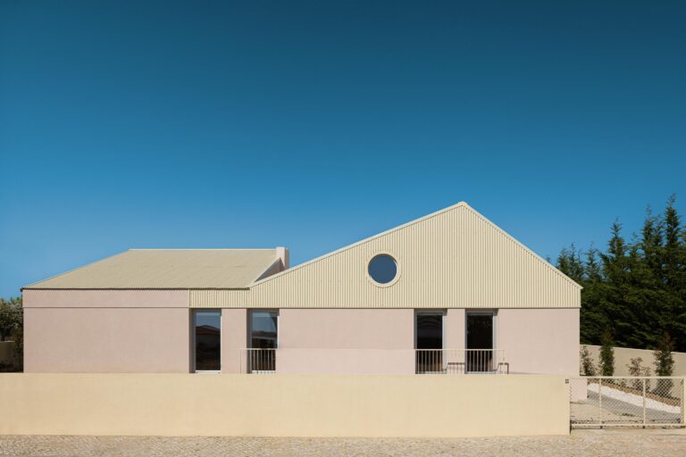 Fachada da moradia com paredes em estuque rosa e cobertura inclinada em chapa metálica bege, com vão circular — Casa do Alpendre arquitectura Vasco Burnay Arquitectura fotografia Ivo Tavares