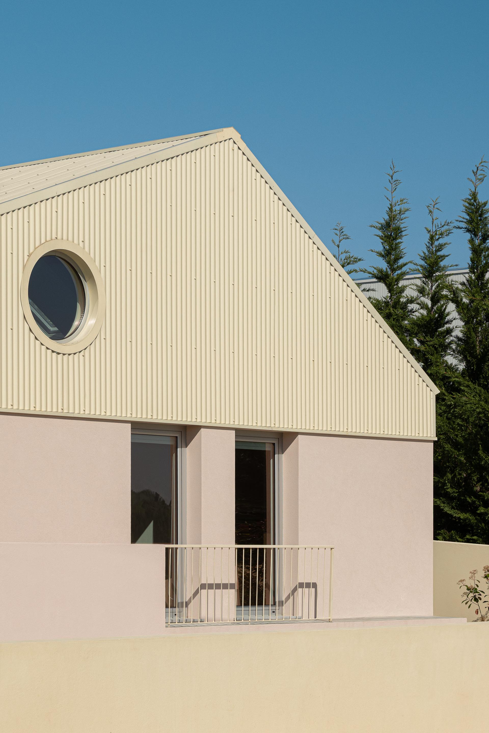 Fachada em estuque rosa com empena revestida a chapa metálica bege, destacando vão circular e varandins — Casa do Alpendre arquitectura Vasco Burnay Arquitectura fotografia Ivo Tavares
