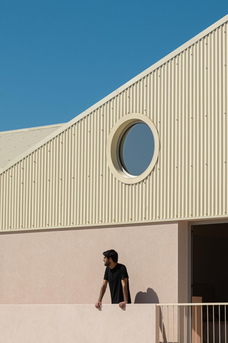 Detalhe da empena revestida a chapa metálica bege com vão circular, e pessoa na varanda — Casa do Alpendre arquitectura Vasco Burnay Arquitectura fotografia Ivo Tavares