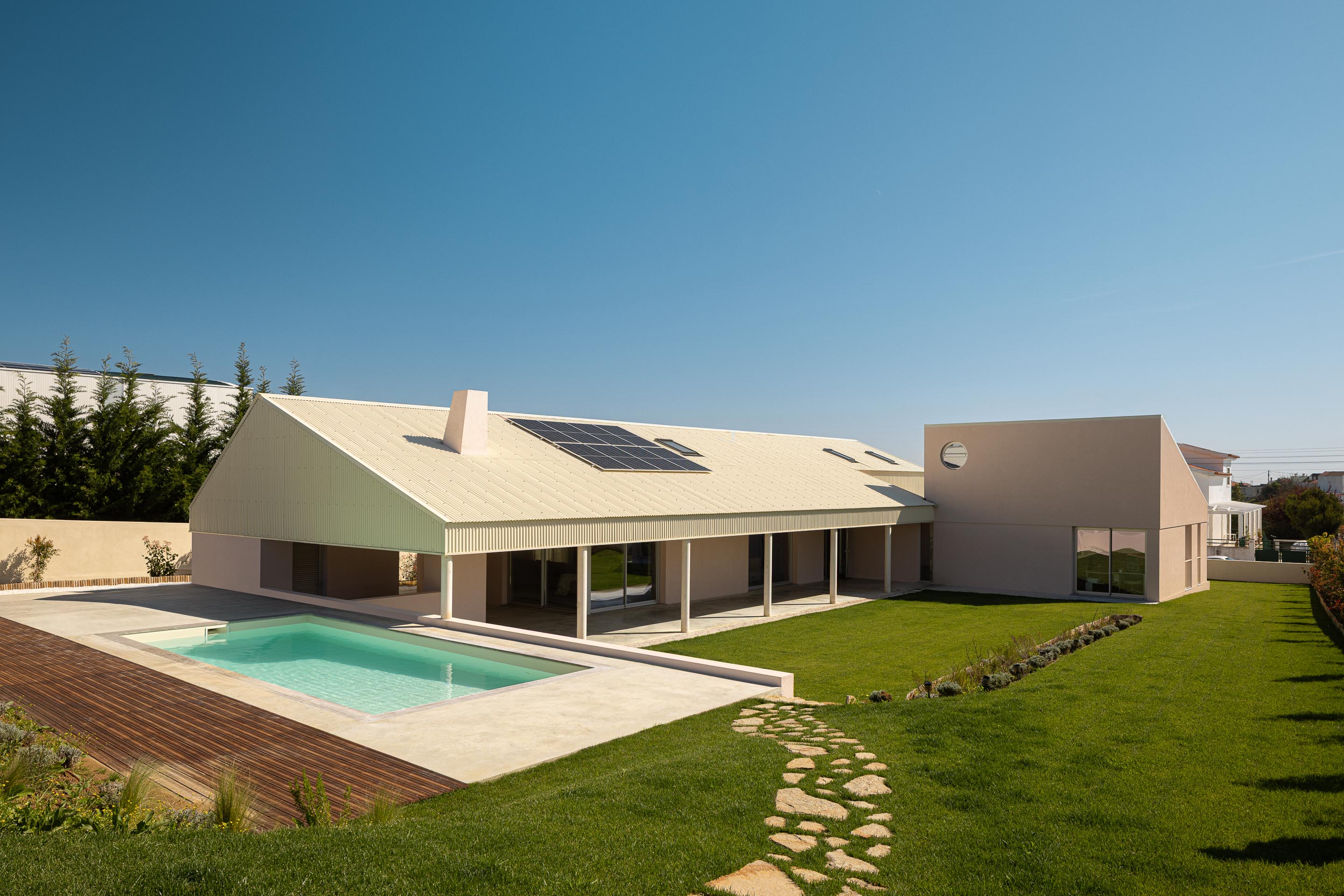 Vista aérea da moradia em L, com cobertura inclinada, piscina e extenso relvado sob céu azul — Casa do Alpendre arquitectura Vasco Burnay Arquitectura fotografia Ivo Tavares