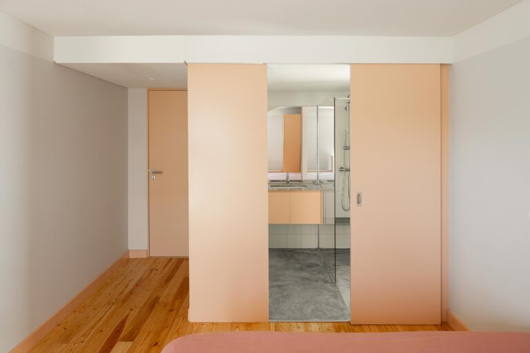 Quarto com pavimento em madeira e porta de correr pêssego, revelando casa de banho adjacente — Casa do Alpendre arquitectura Vasco Burnay Arquitectura fotografia Ivo Tavares