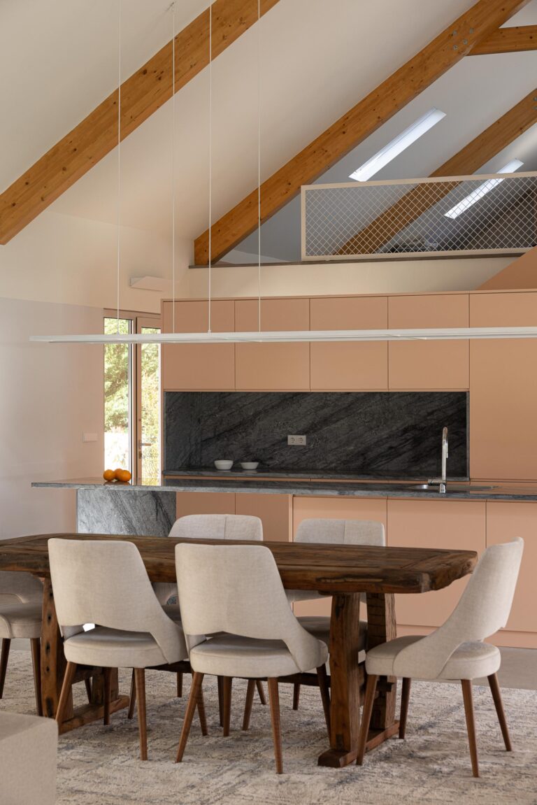 Detalhe da cozinha com bancada em mármore escuro, armários pêssego e mesa de jantar em madeira — Casa do Alpendre arquitectura Vasco Burnay Arquitectura fotografia Ivo Tavares