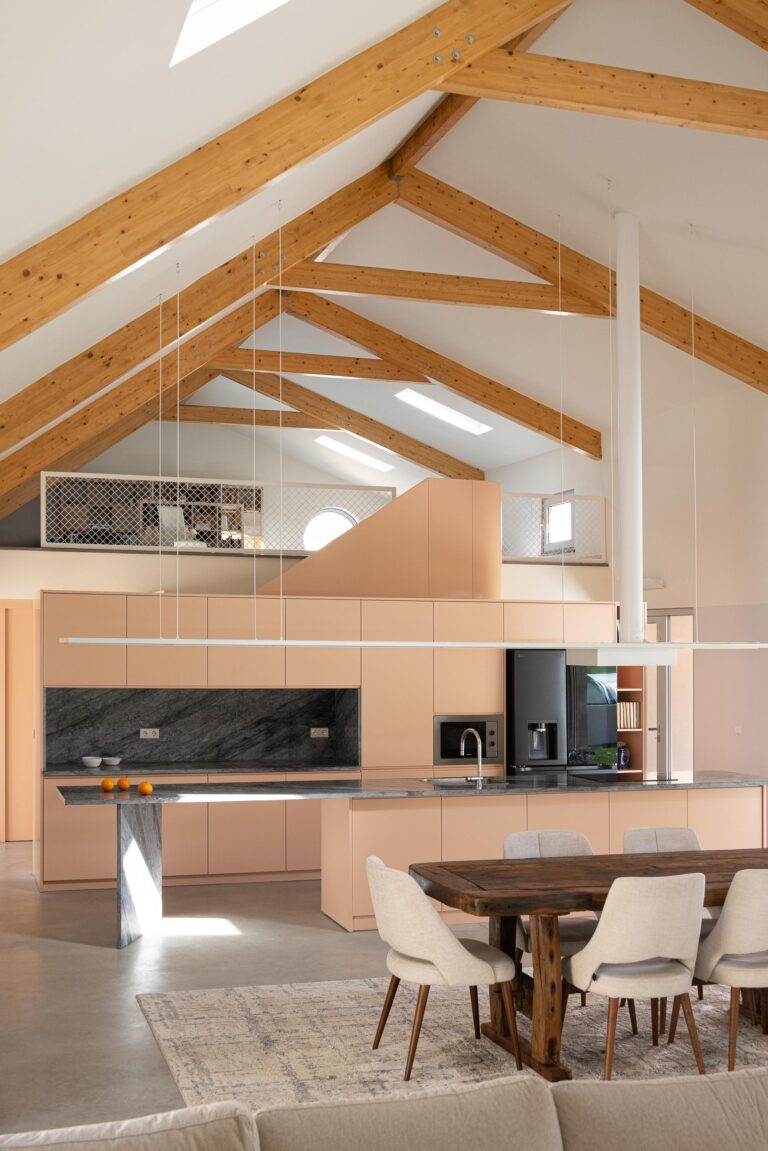 Cozinha com bancadas em mármore escuro e armários pêssego, com sótão habitável visível acima — Casa do Alpendre arquitectura Vasco Burnay Arquitectura fotografia Ivo Tavares