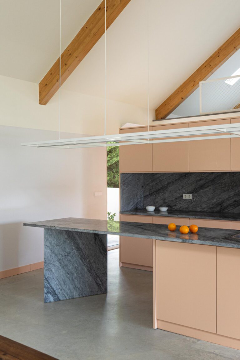Cozinha com ilha central em mármore escuro e armários pêssego, sob luz natural — Casa do Alpendre arquitectura Vasco Burnay Arquitectura fotografia Ivo Tavares