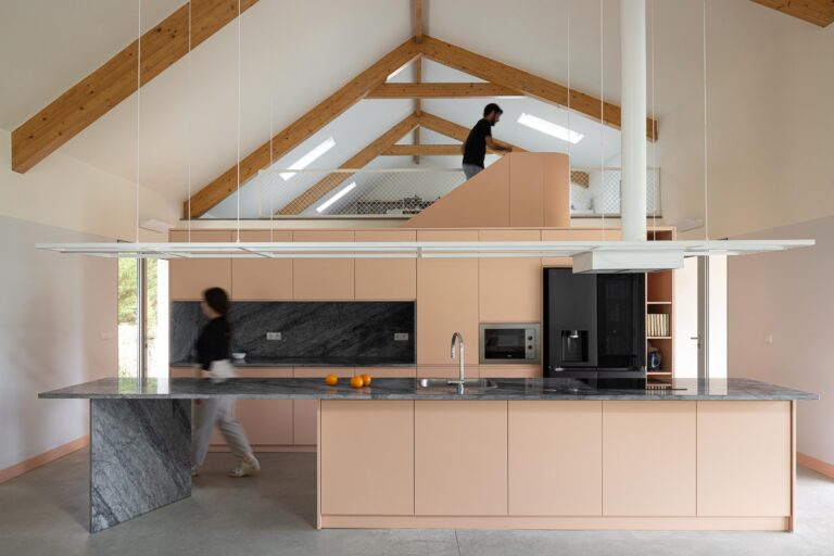 Cozinha com ilha e bancadas em mármore, armários pêssego, e pessoa no sótão — Casa do Alpendre arquitectura Vasco Burnay Arquitectura fotografia Ivo Tavares