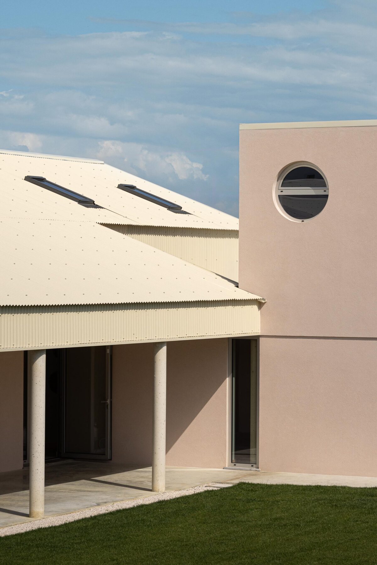 Vista exterior da moradia em L, com alpendre e paredes em estuque rosa, sob céu parcialmente nublado — Casa do Alpendre arquitectura Vasco Burnay Arquitectura fotografia Ivo Tavares