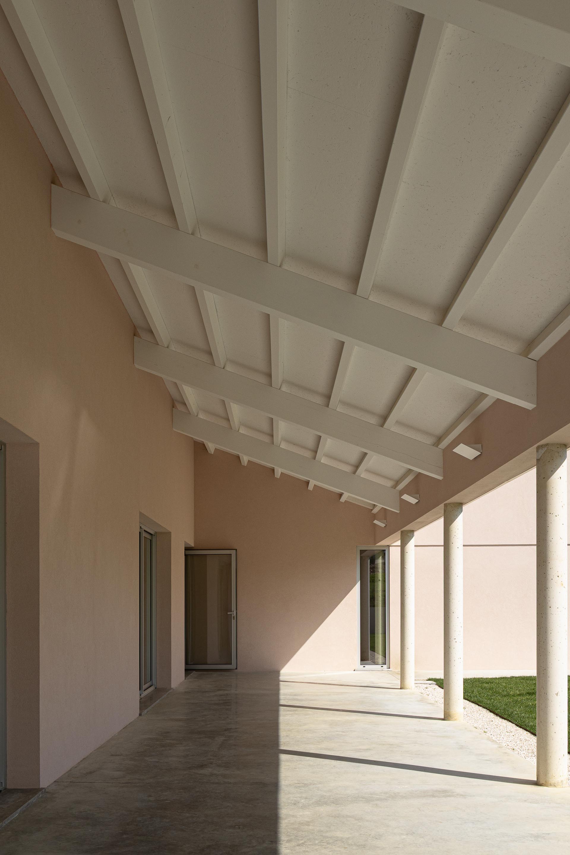 Interior do alpendre com estrutura de madeira da cobertura exposta, paredes rosa e pavimento em betão — Casa do Alpendre arquitectura Vasco Burnay Arquitectura fotografia Ivo Tavares