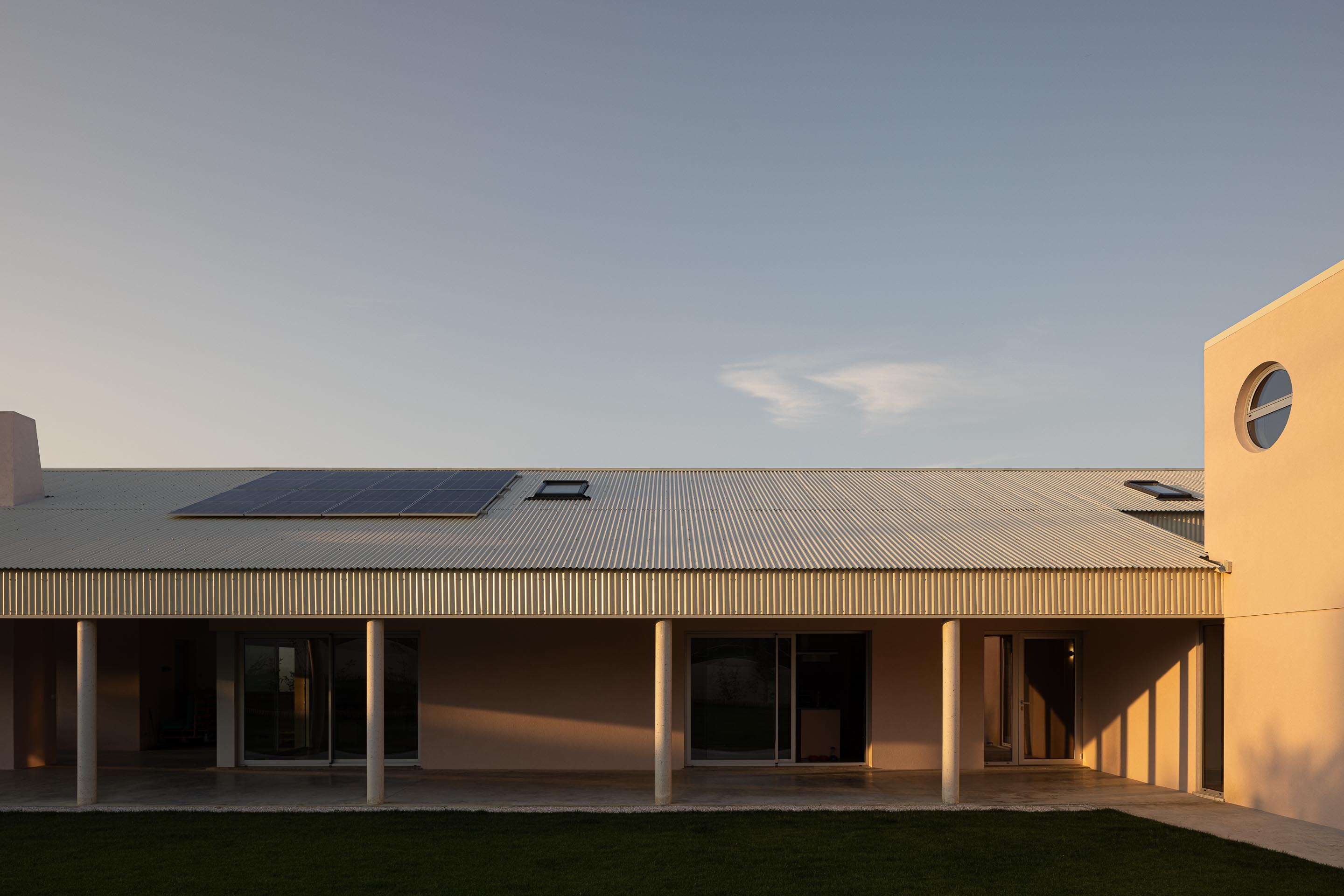 Moradia com alpendre e volume curto, iluminados pela luz do pôr do sol, com painéis solares — Casa do Alpendre arquitectura Vasco Burnay Arquitectura fotografia Ivo Tavares
