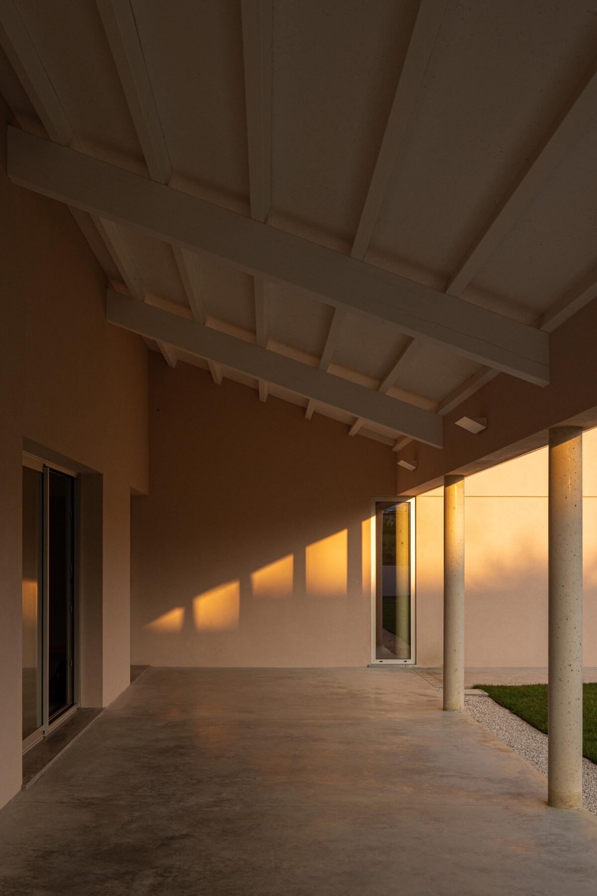 Interior do alpendre com estrutura de madeira exposta e pavimento em betão, sob luz do pôr do sol — Casa do Alpendre arquitectura Vasco Burnay Arquitectura fotografia Ivo Tavares